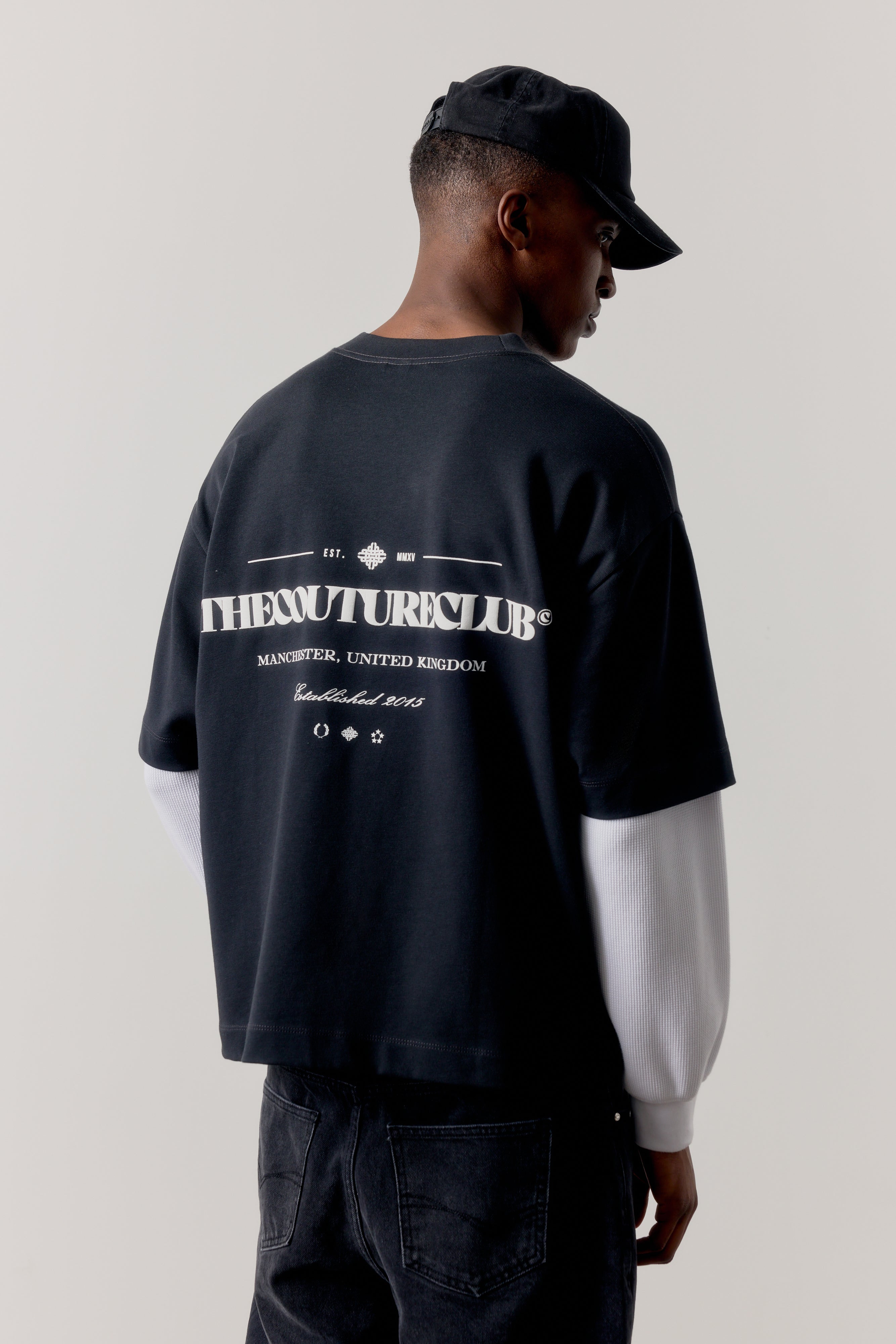 Person wearing a black oversized sweatshirt with branded text on the back against a plain background