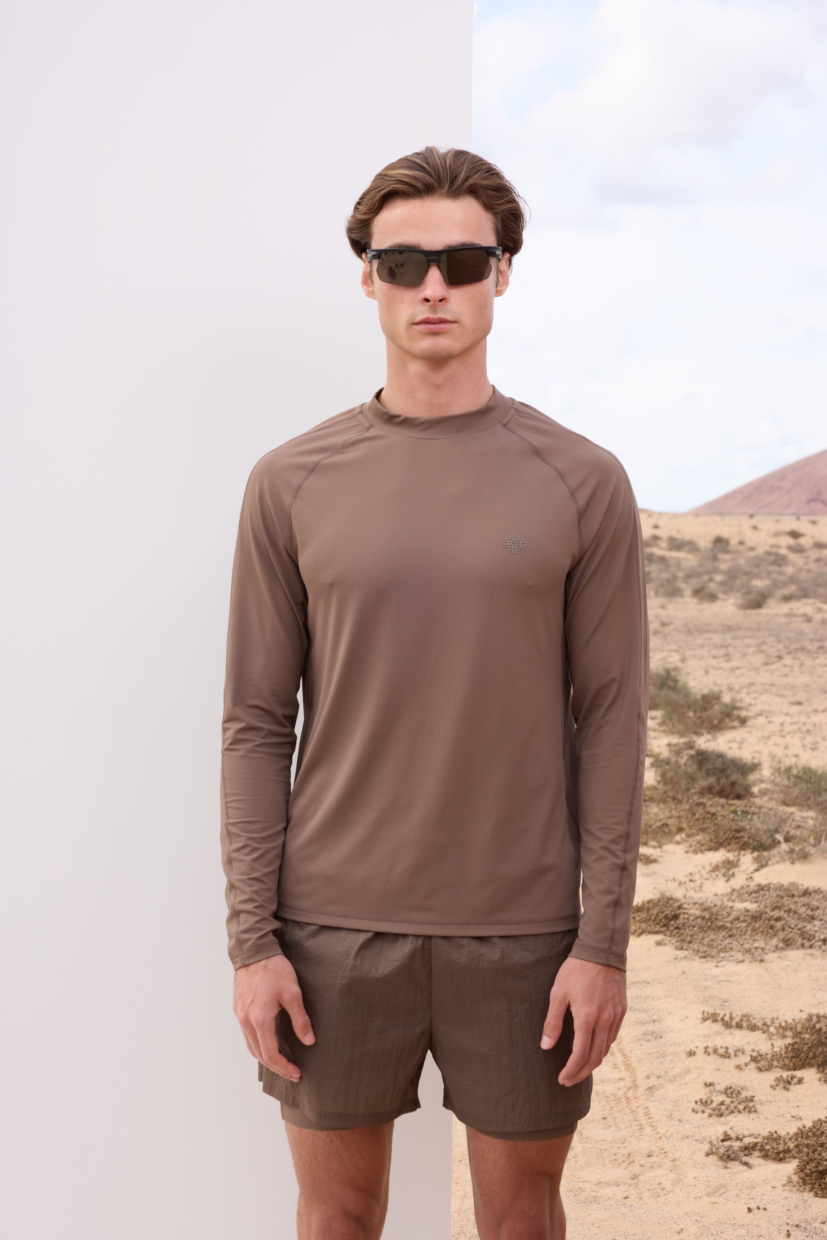 Man wearing a brown long-sleeve t-shirt and shorts standing in a desert landscape.