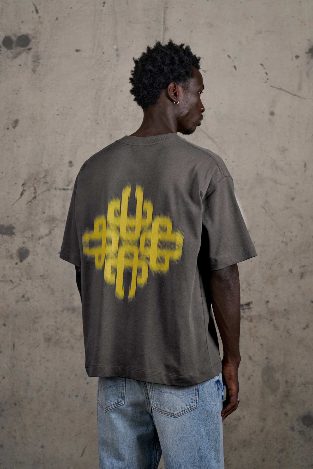 Model wearing the Motion Blurred Emblem T-Shirt in Charcoal/Yellow, back view