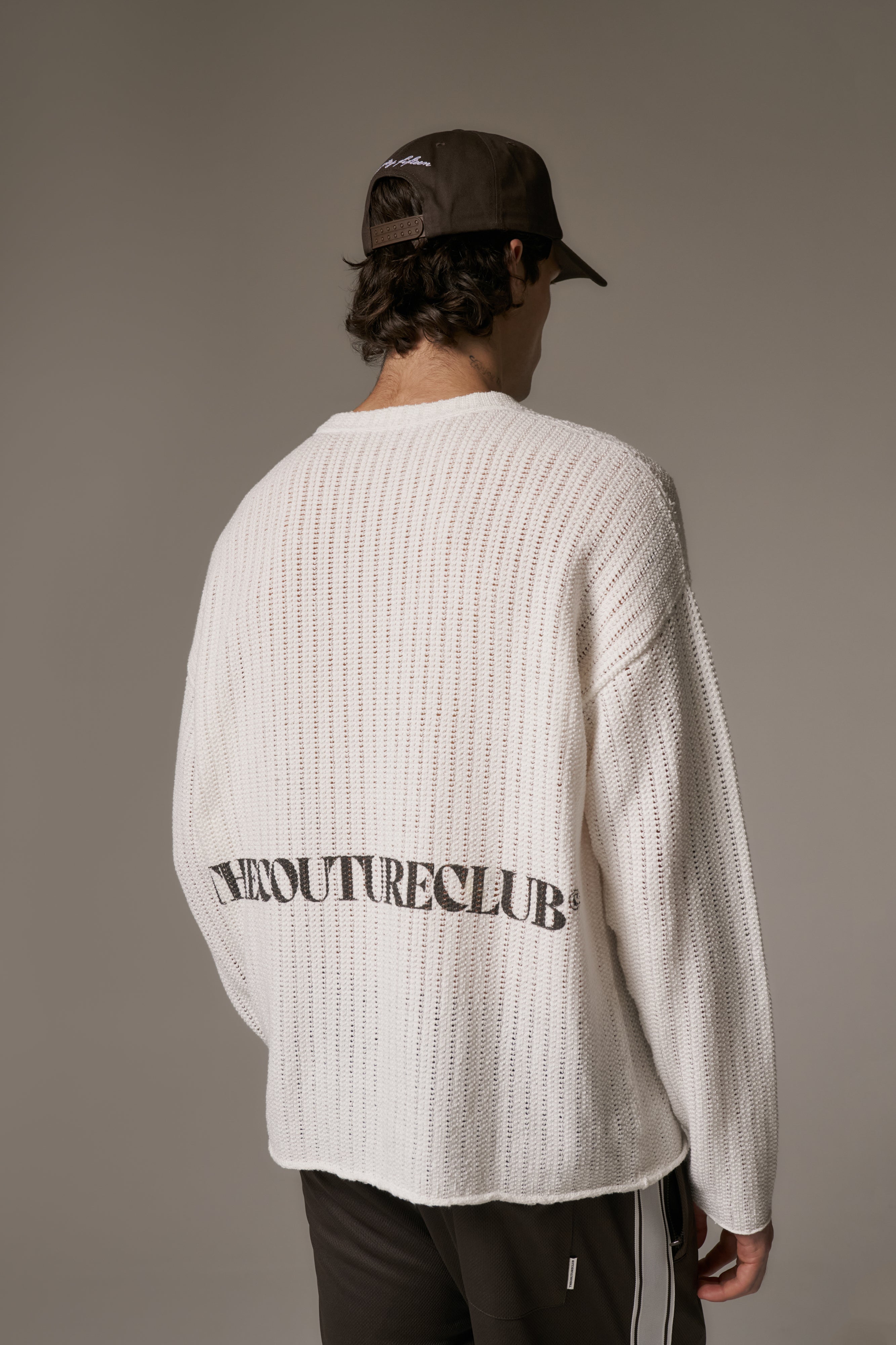 Person wearing a white long-sleeve crochet t-shirt with branded text on the back, standing against a plain background.