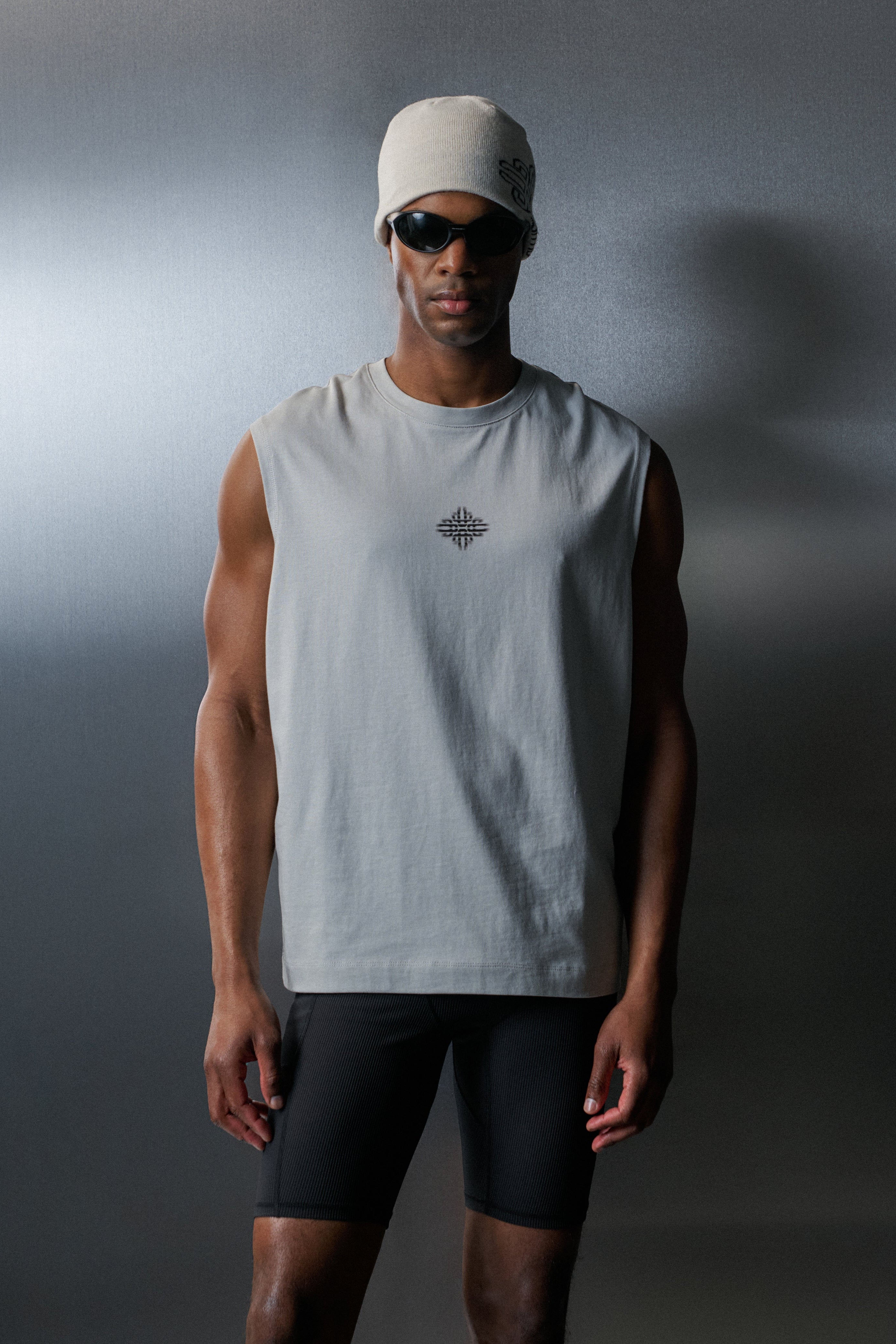 Man wearing a light grey vest and black shorts against a dark background