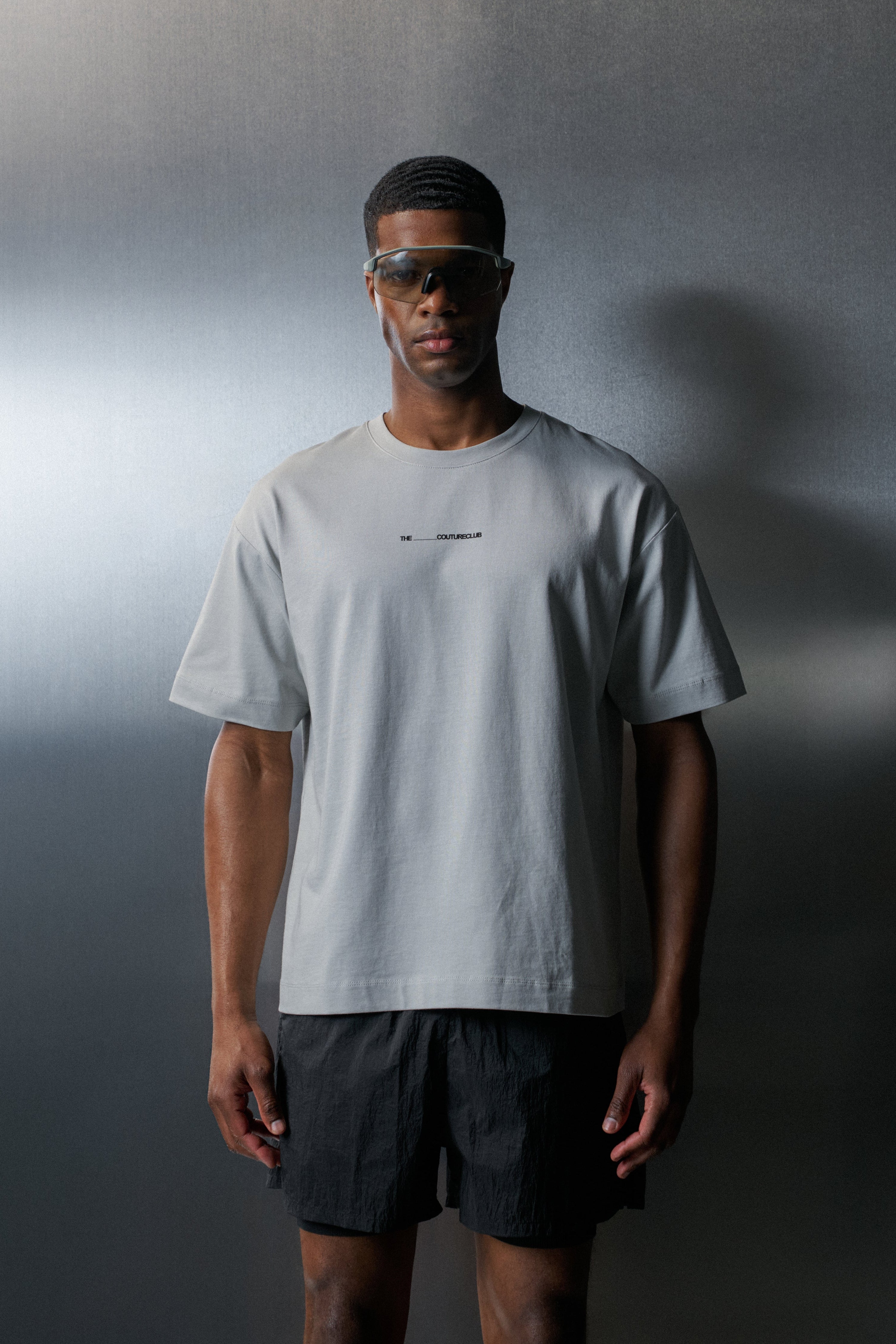 Man wearing a light grey t-shirt and black shorts against a dark background