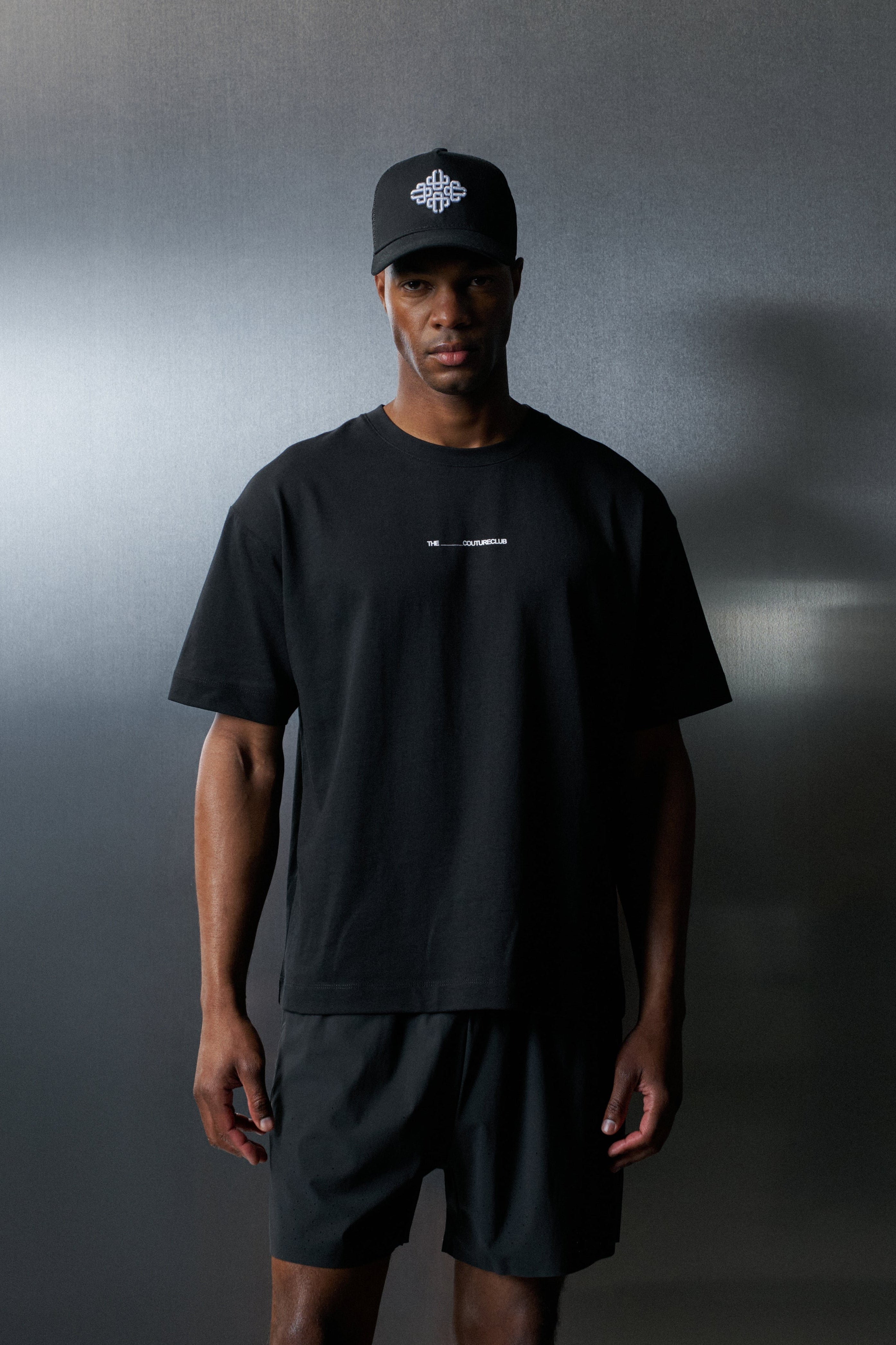 Man wearing a black t-shirt and shorts with a cap against a dark background