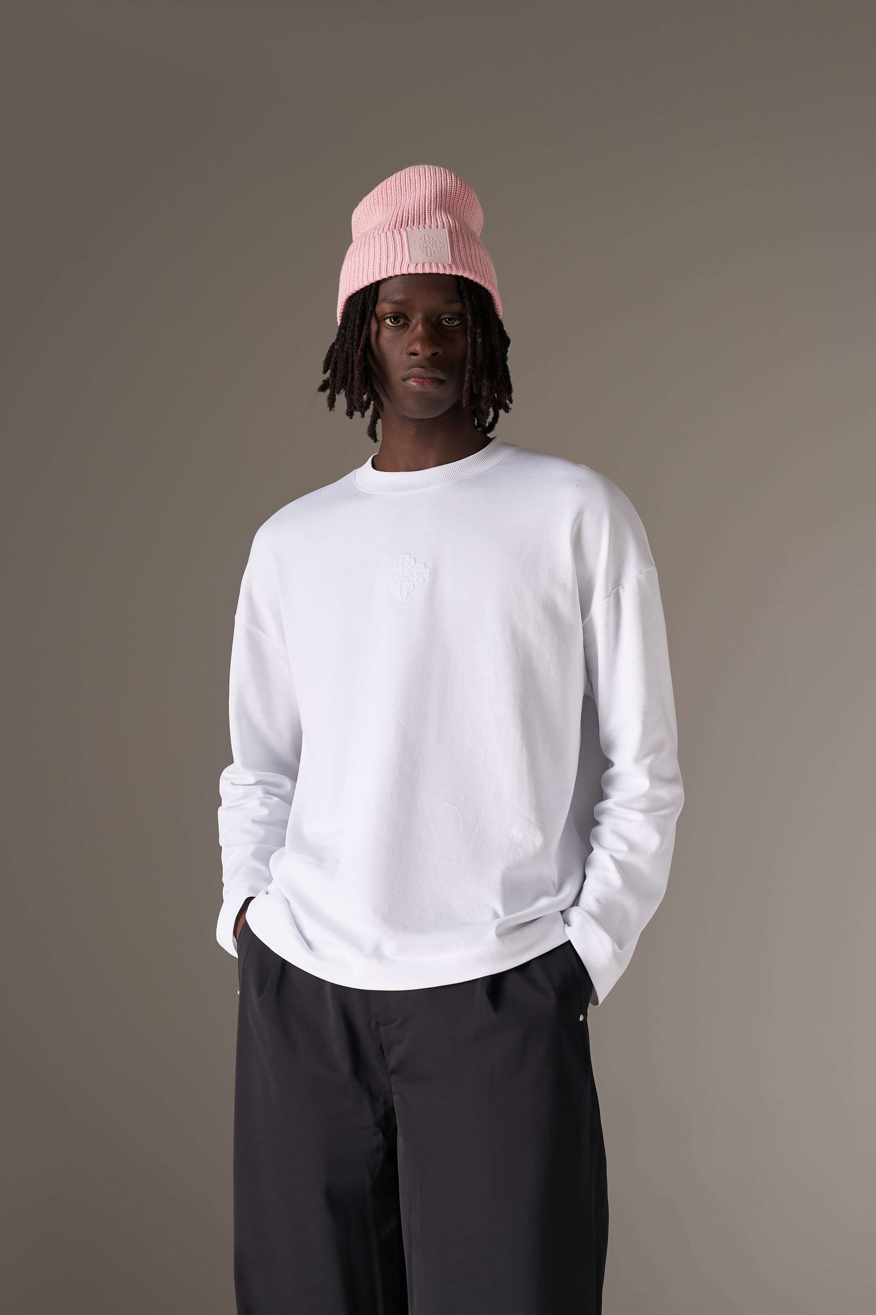 Person wearing a white long sleeve t-shirt and black pants with a pink beanie on a grey background