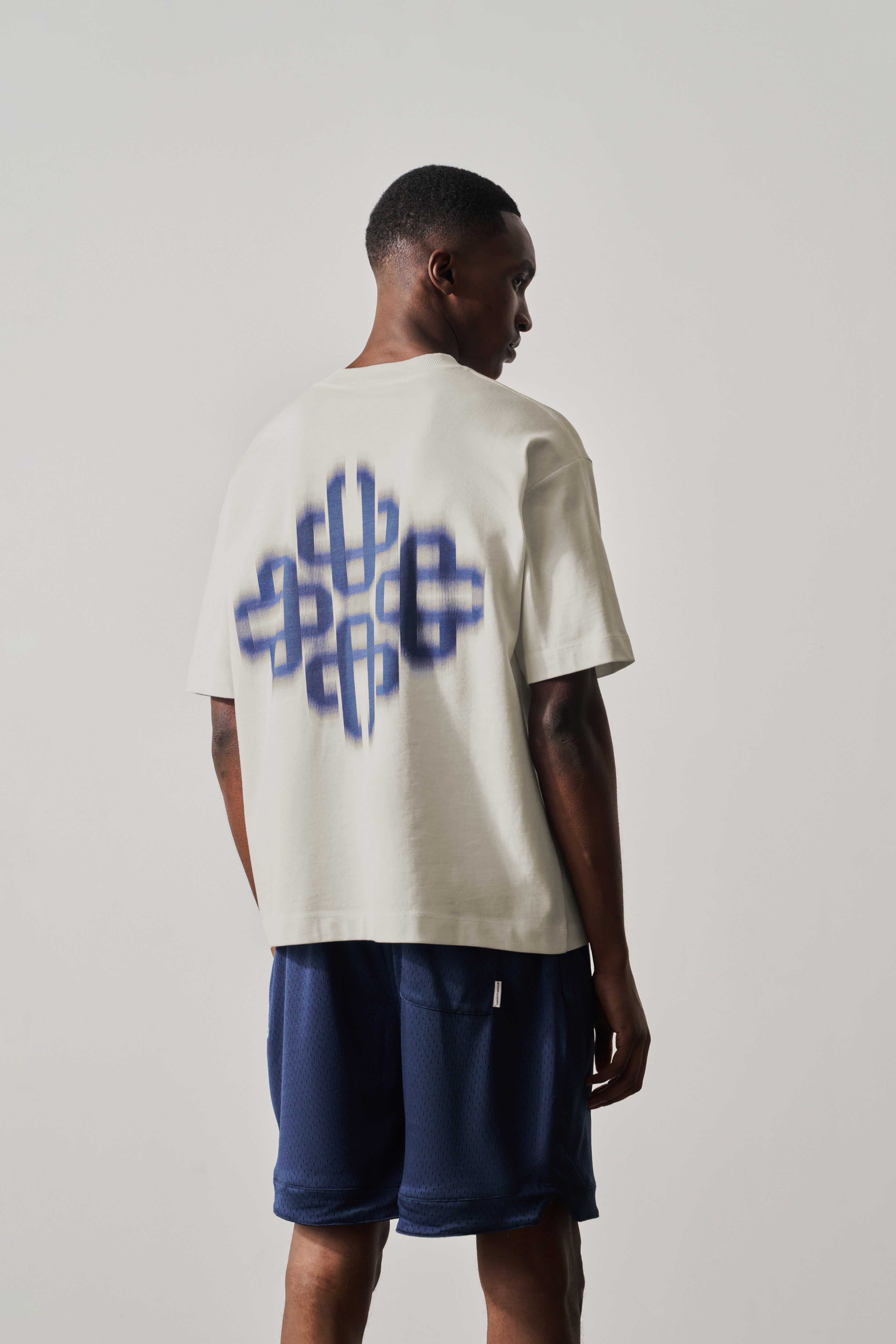 Person wearing a white t-shirt with a blue graphic design on the back, standing against a plain background.