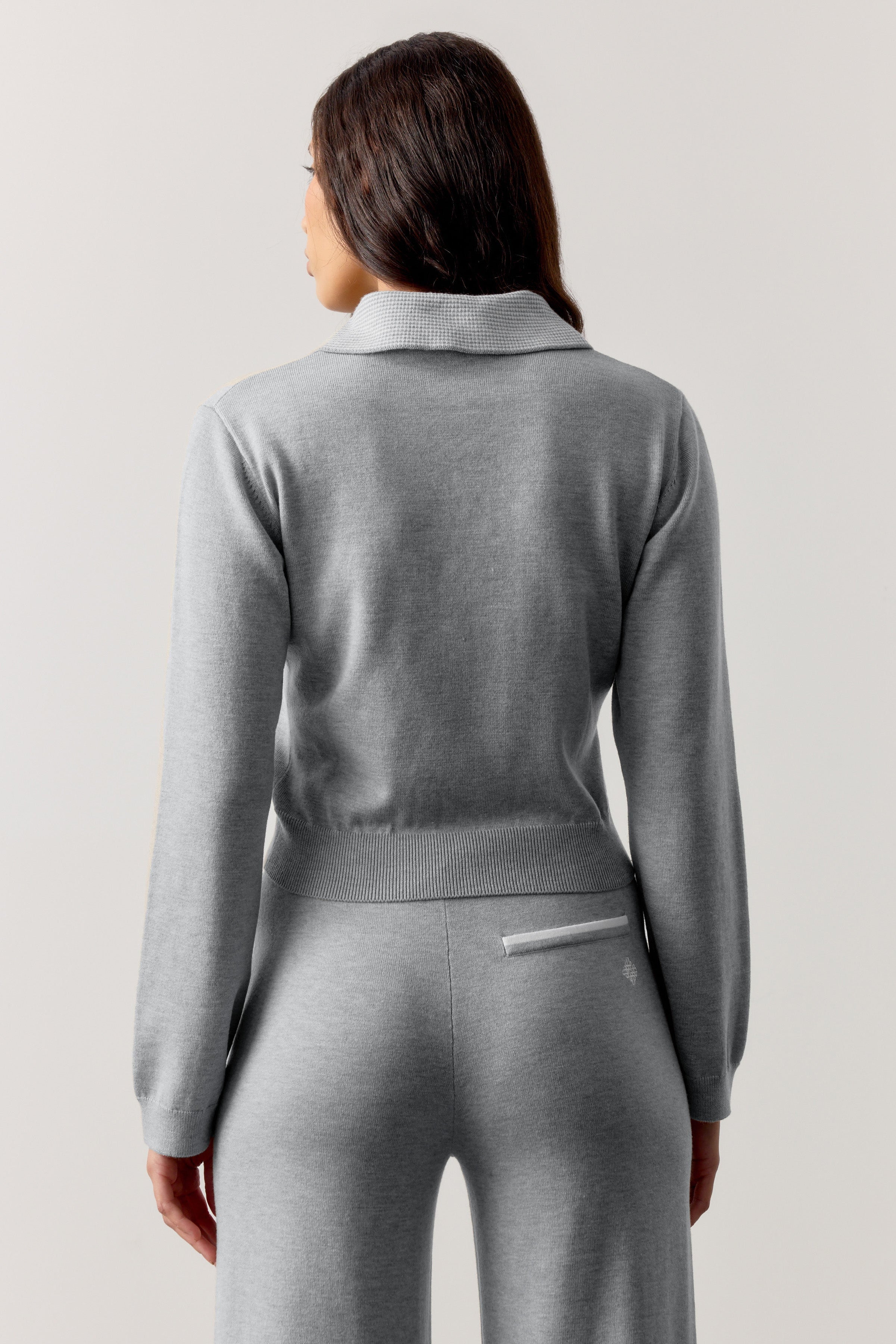Woman wearing a grey long sleeved polo top with a plain background