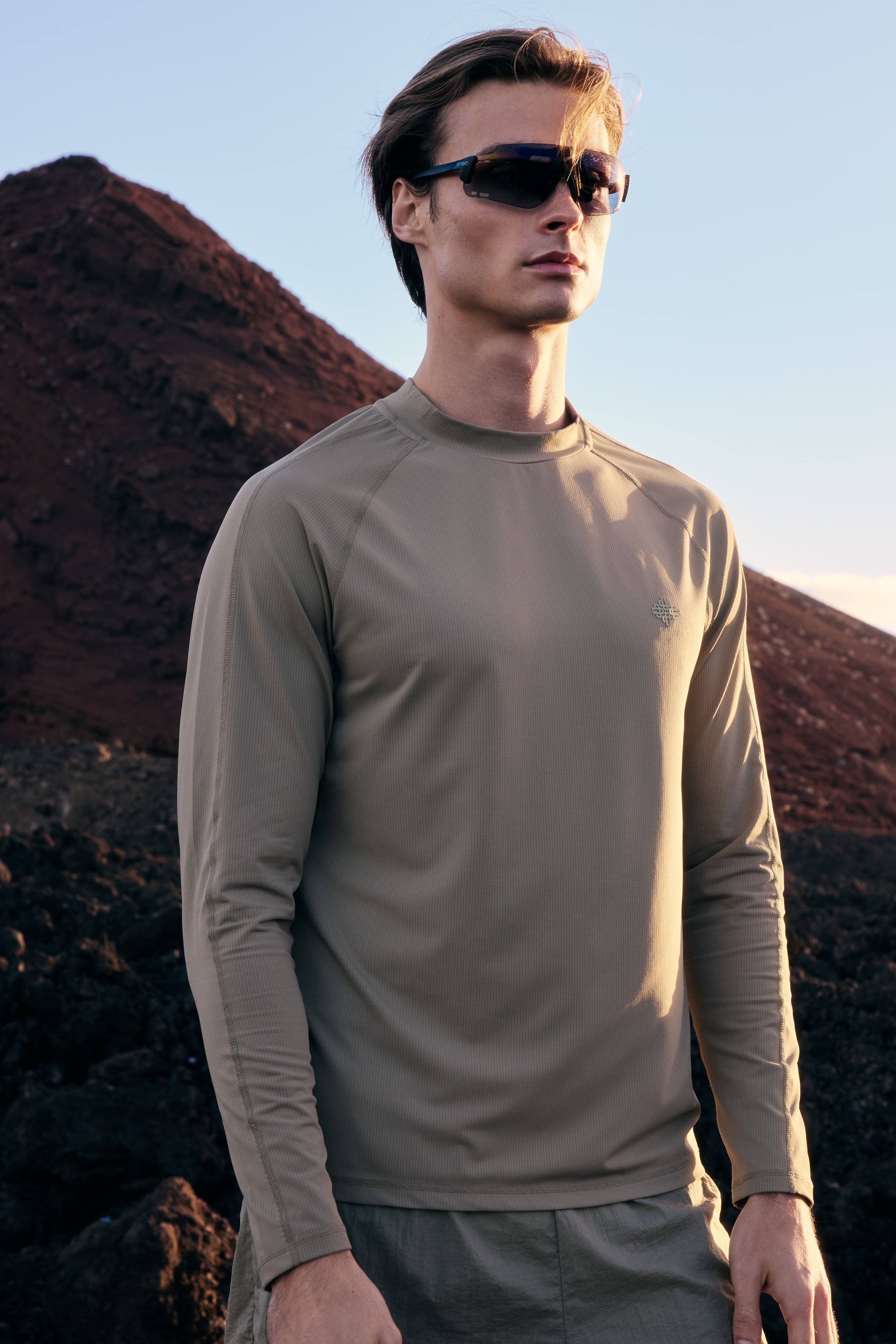 Man wearing a khaki long-sleeve t-shirt and sunglasses in a desert landscape