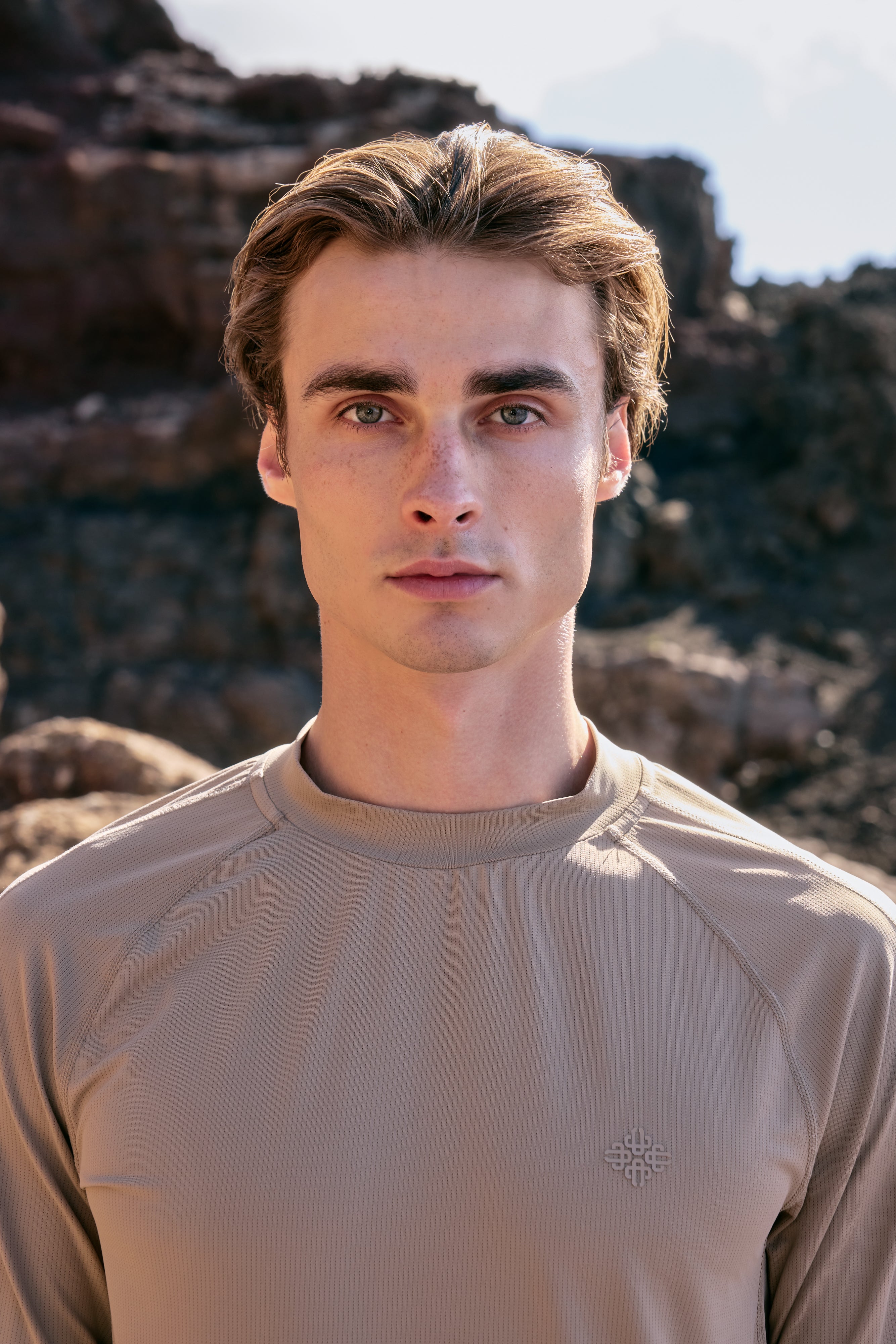 Man wearing a beige long-sleeve t-shirt against a rocky background
