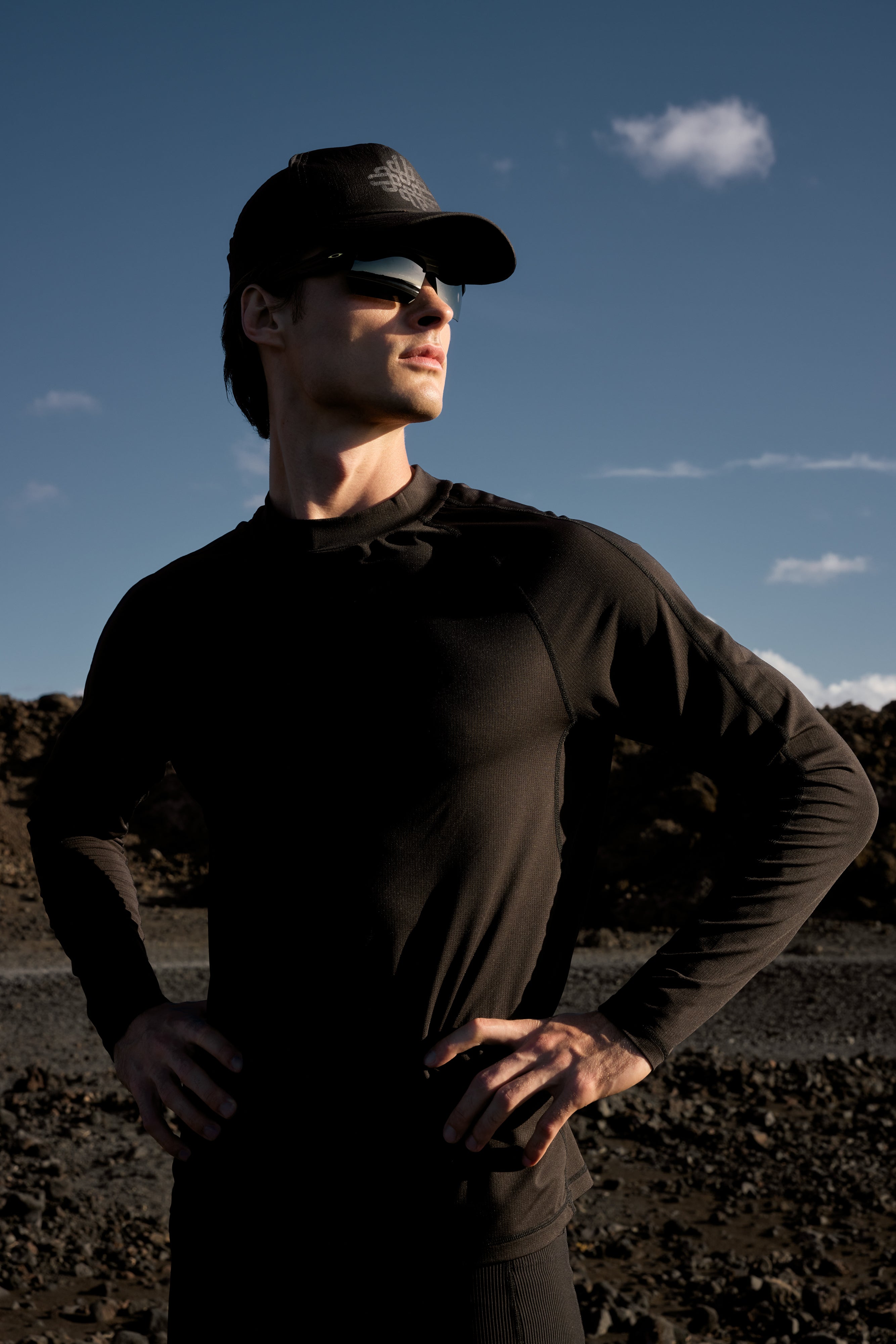 Man wearing sunglasses and a cap standing in a desert landscape with a clear sky.