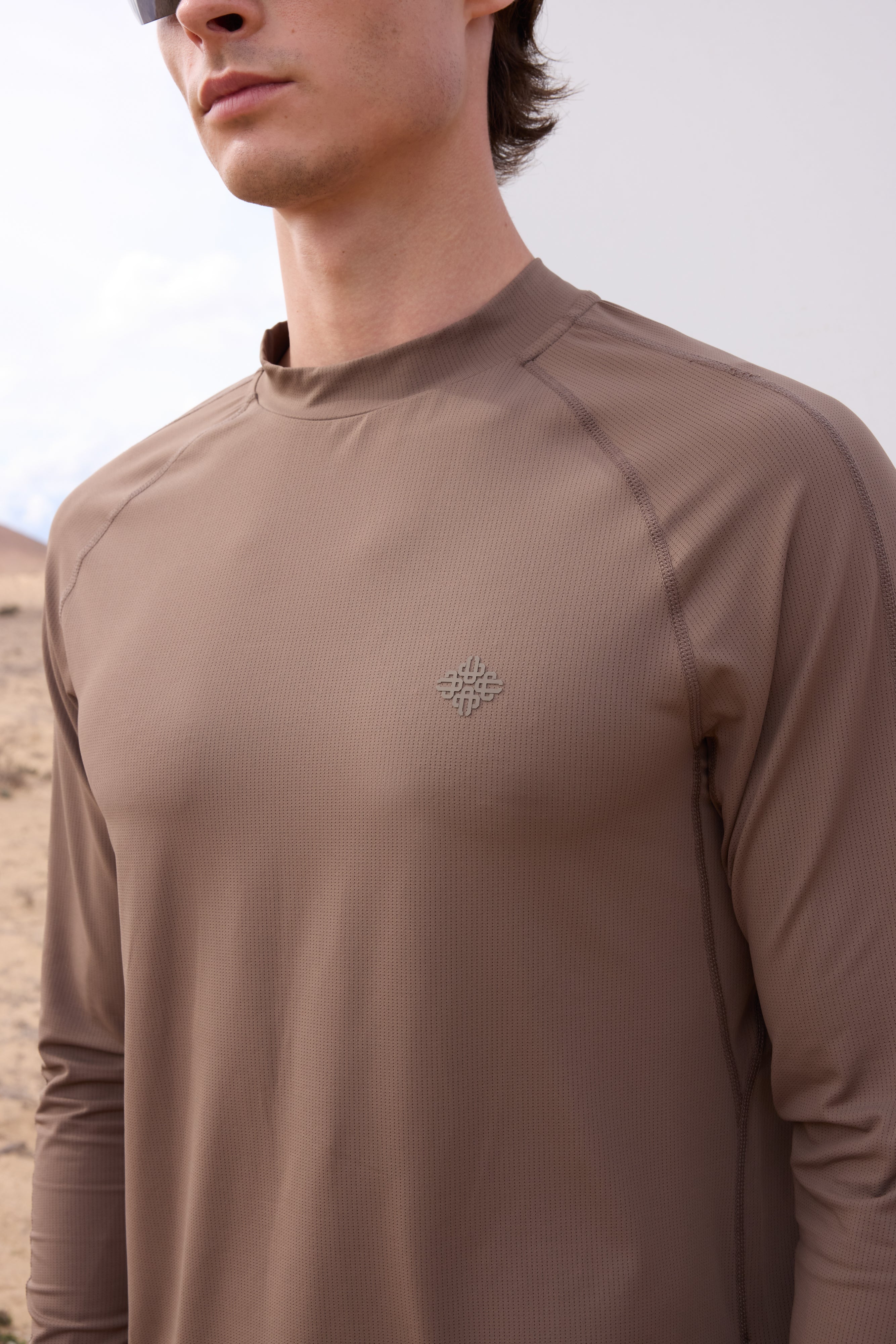 Man wearing a brown long-sleeve t-shirt with a logo against a desert background
