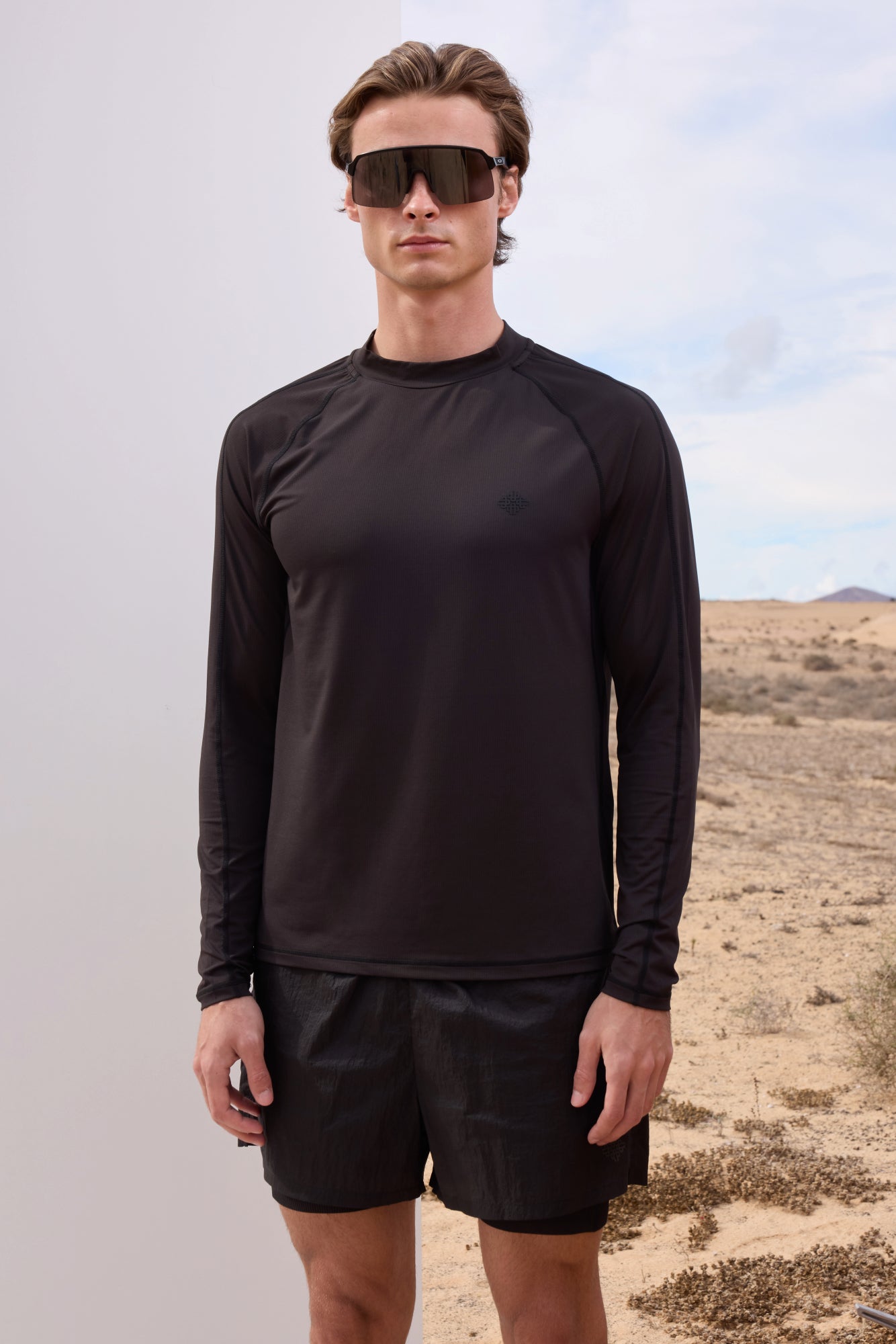 Man wearing a black long-sleeve shirt and shorts standing in a desert landscape.