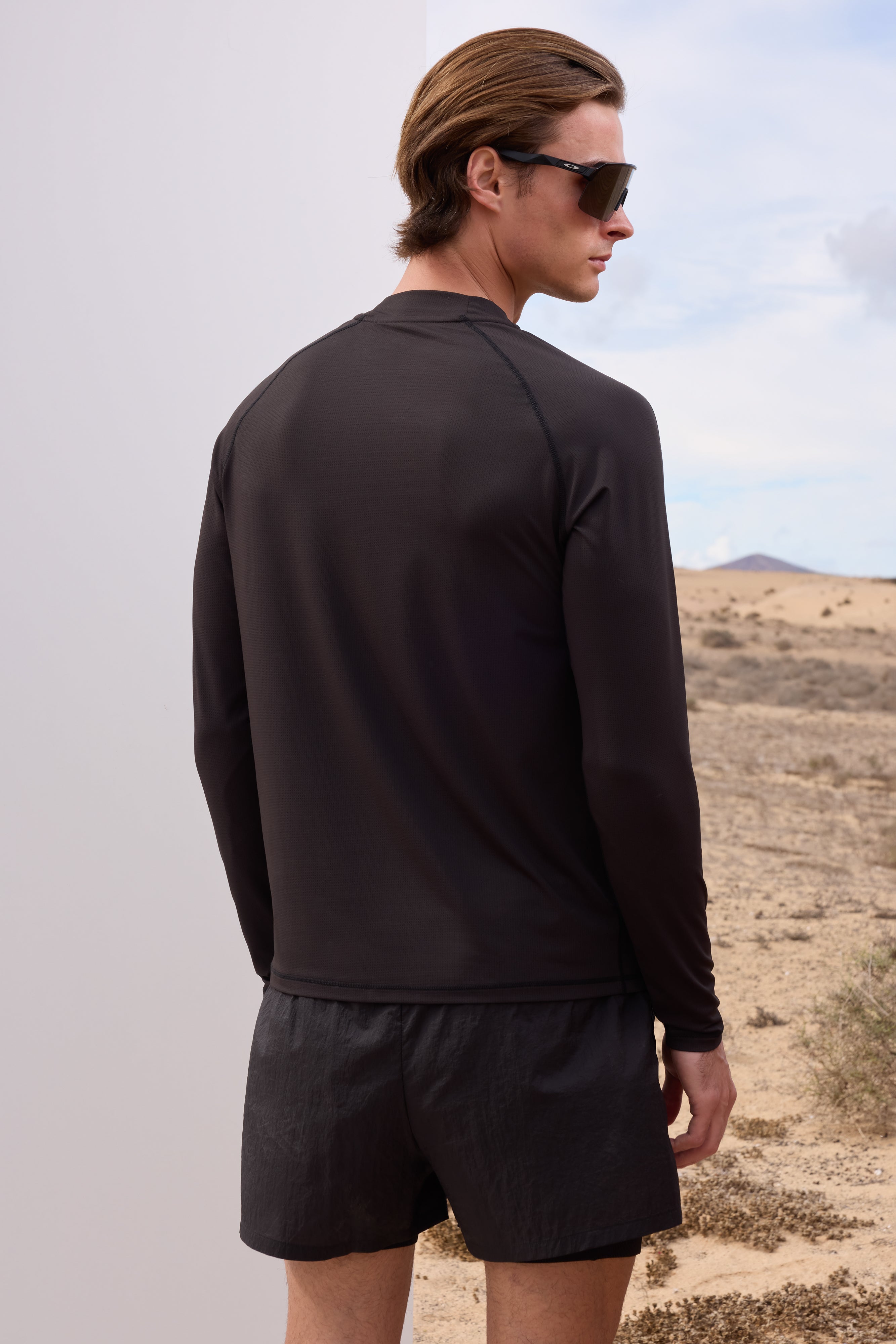 Man wearing a black long-sleeve t-shirt and shorts standing in a desert landscape.