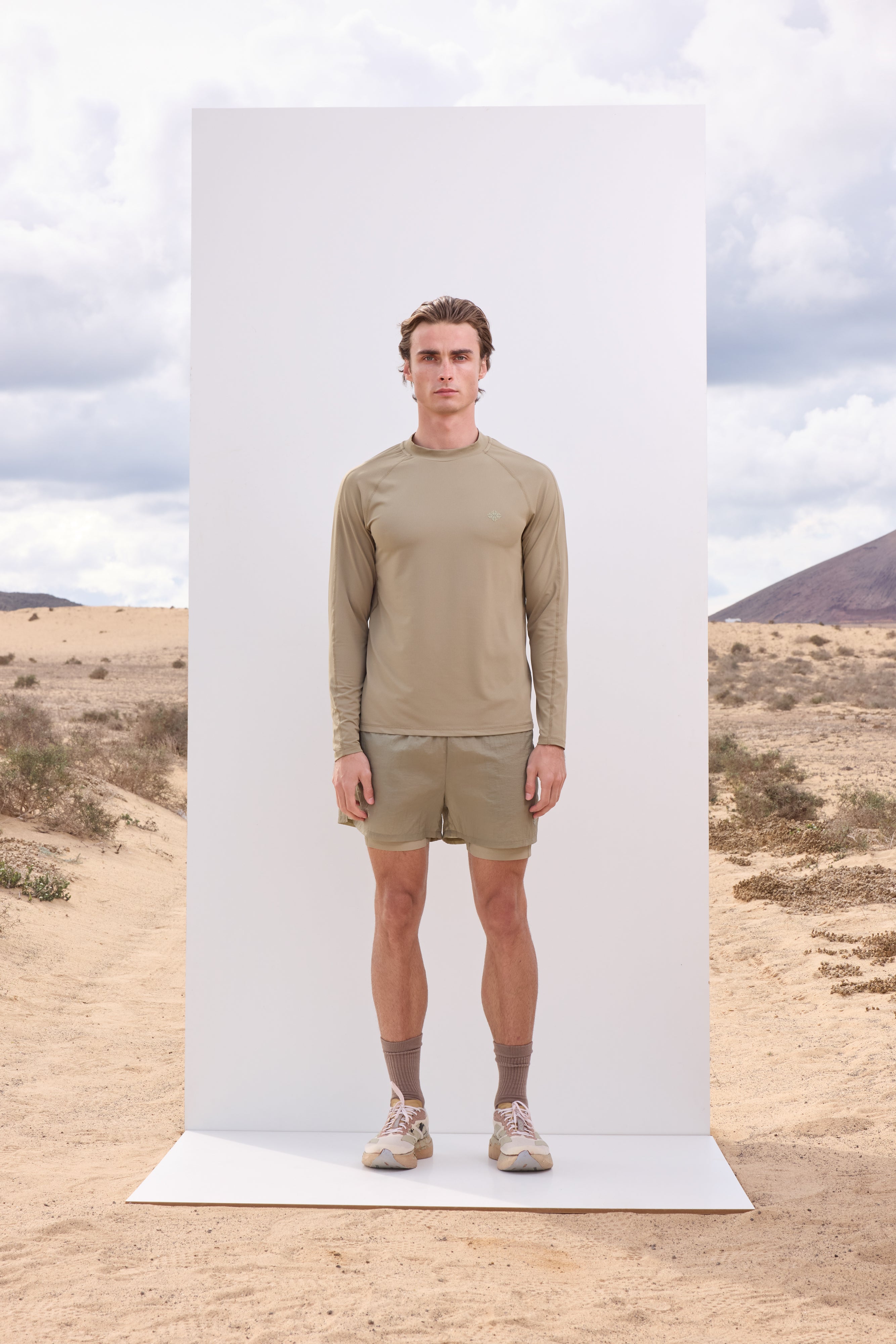 Man wearing a khaki long-sleeve t-shirt and shorts standing in a desert landscape.