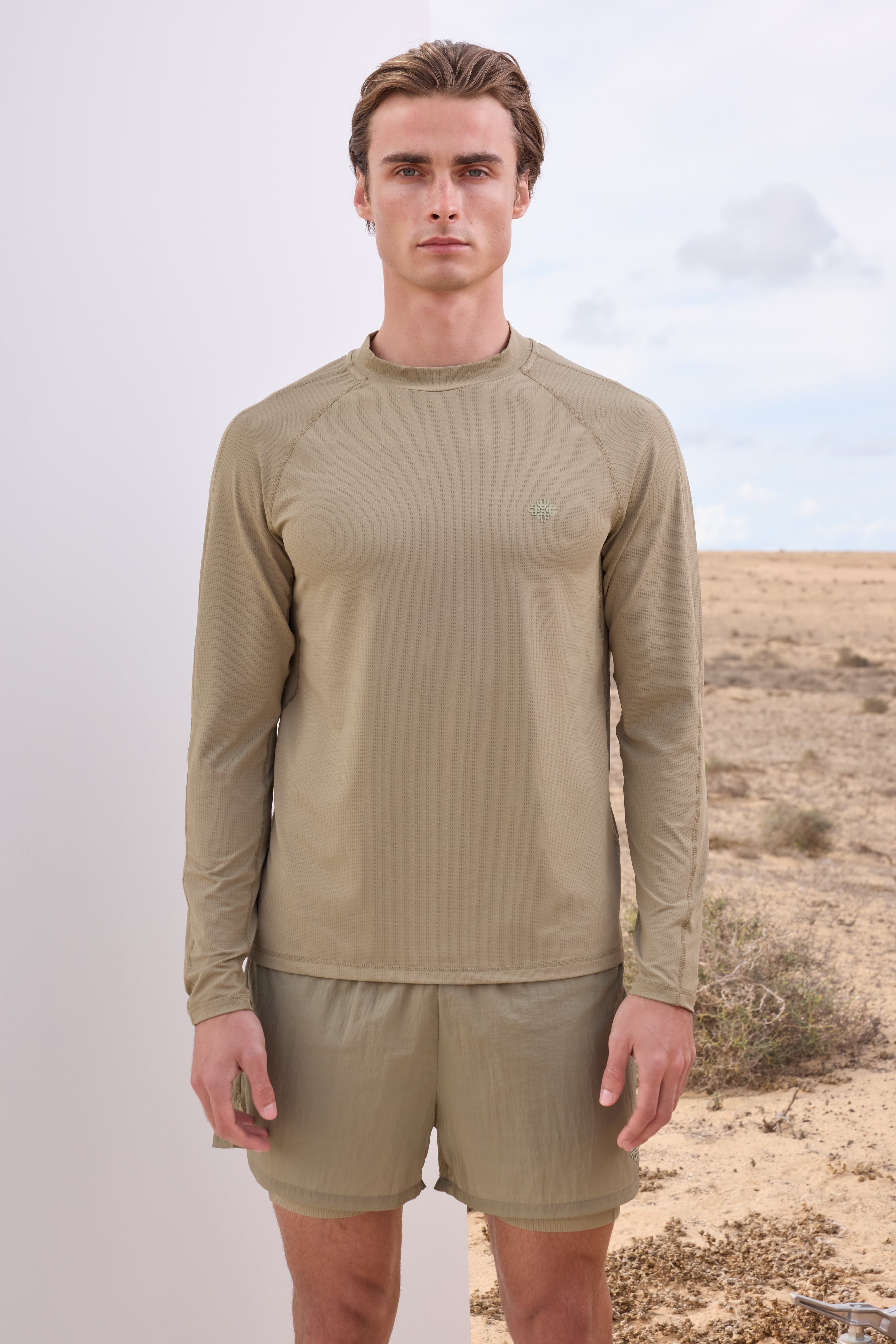 Man wearing a beige long-sleeve t-shirt and shorts in a desert setting