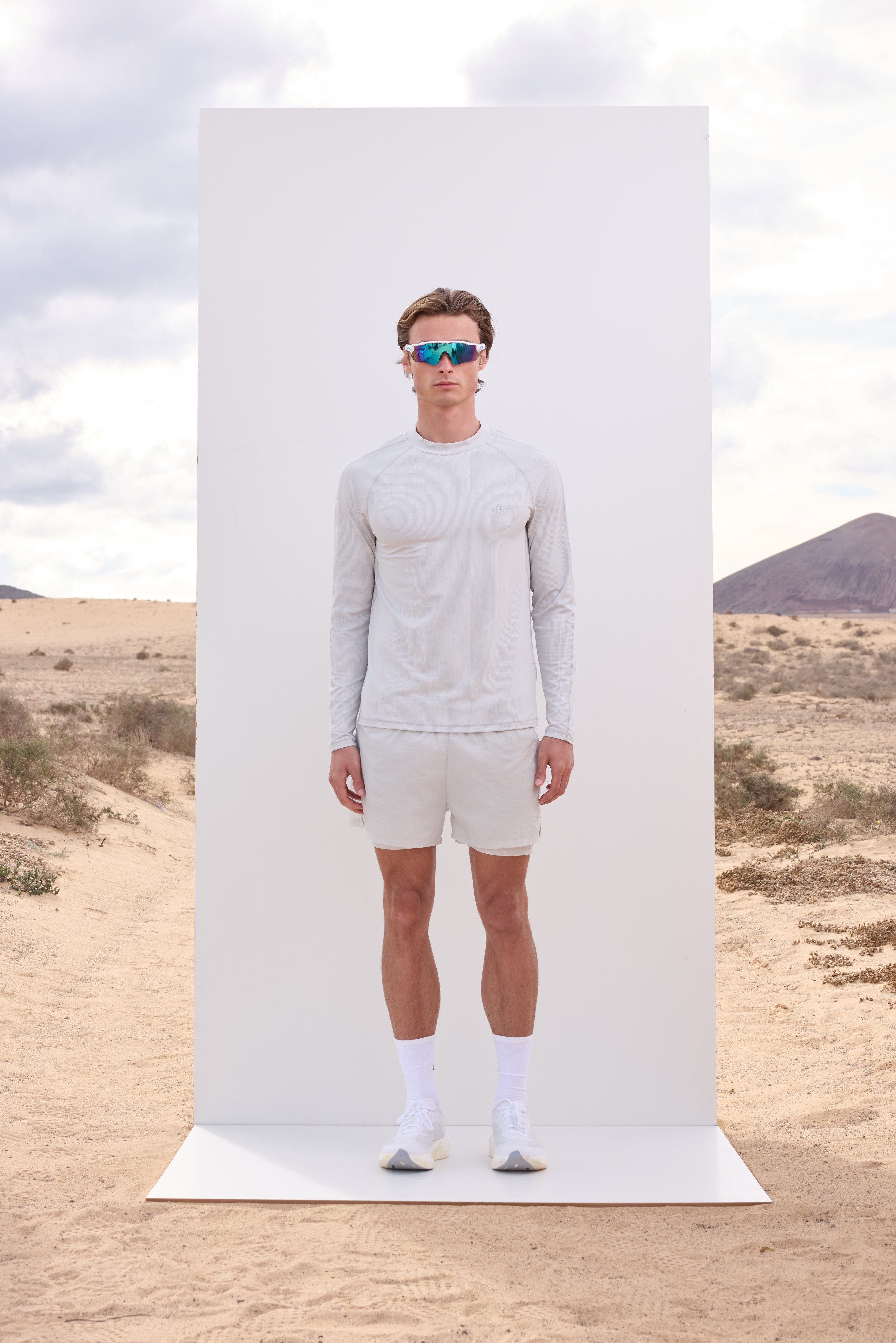 Man in light grey long-sleeve t-shirt and white shorts standing on a desert landscape with a white rectangular platform.