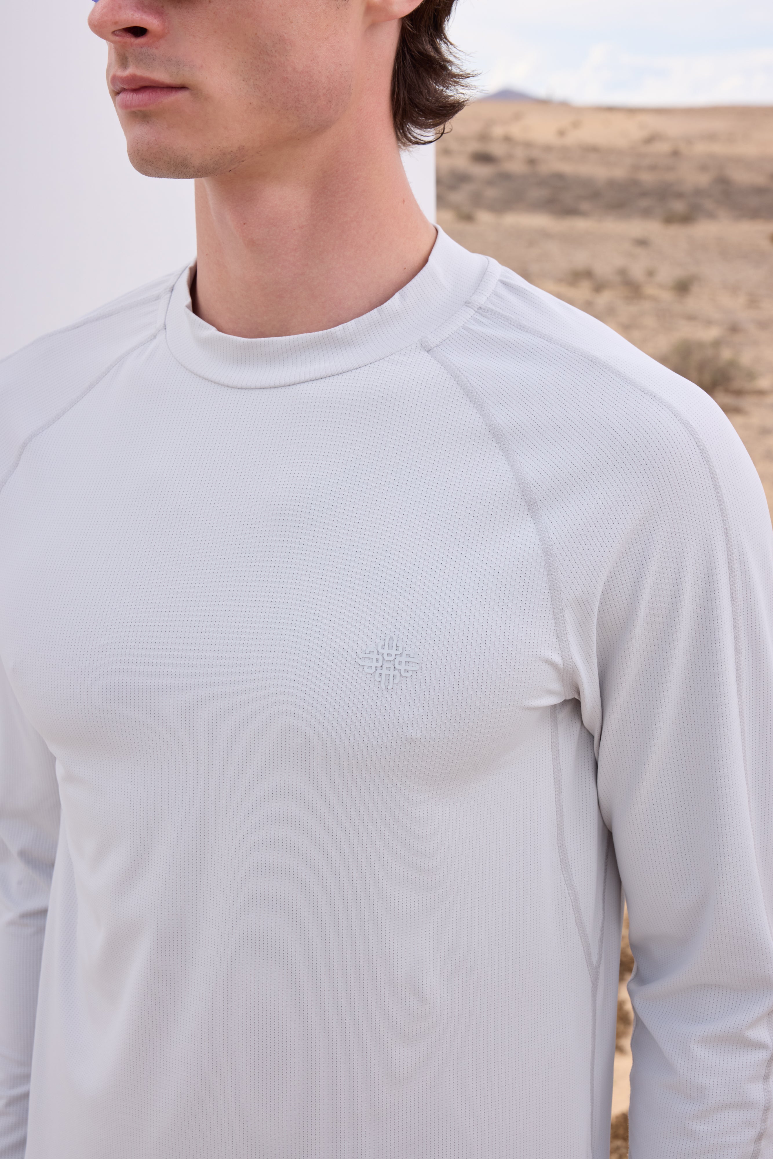 Person wearing a light grey long-sleeve t-shirt with a logo on a desert background