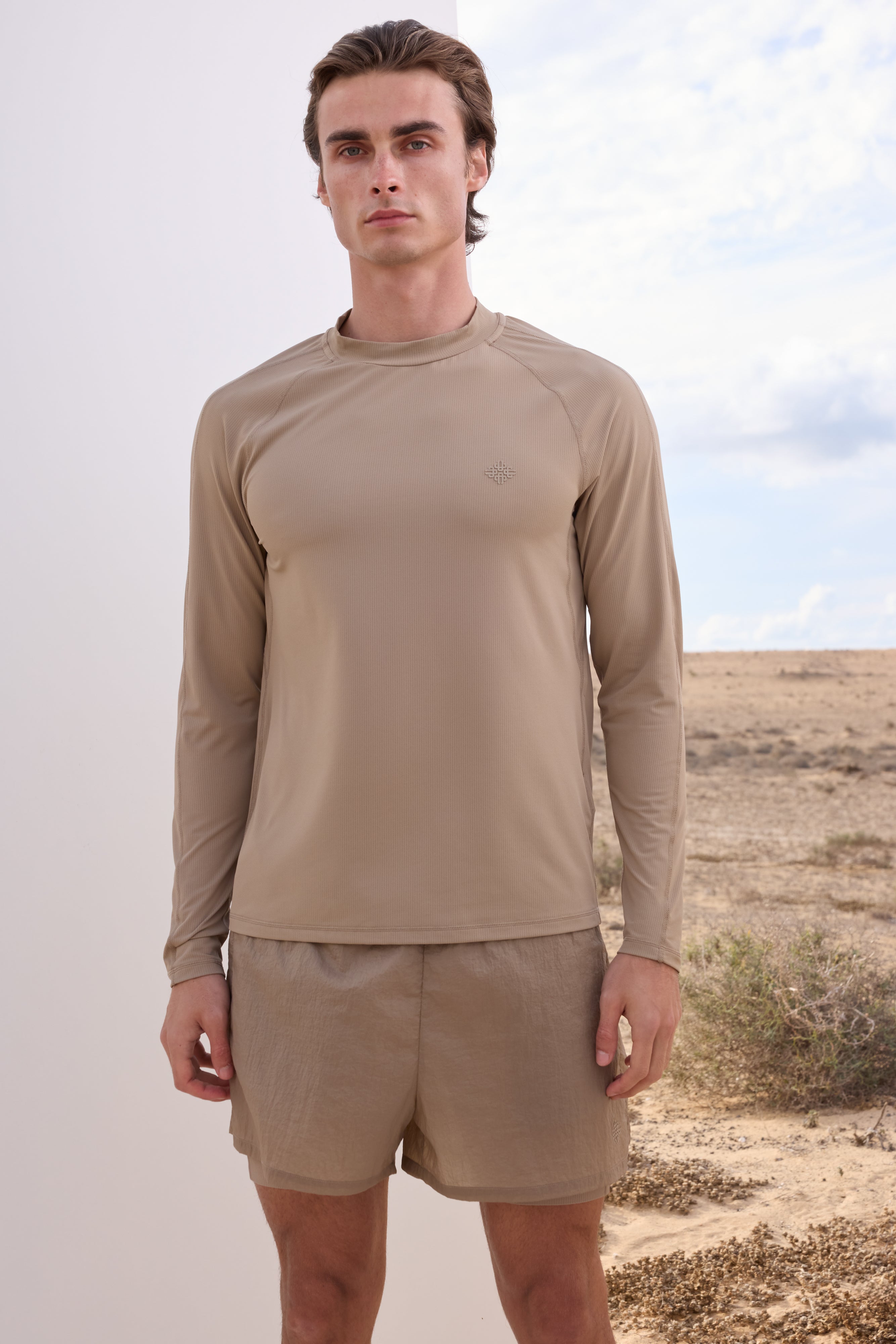 Man wearing a beige long-sleeve t-shirt and shorts in a desert setting