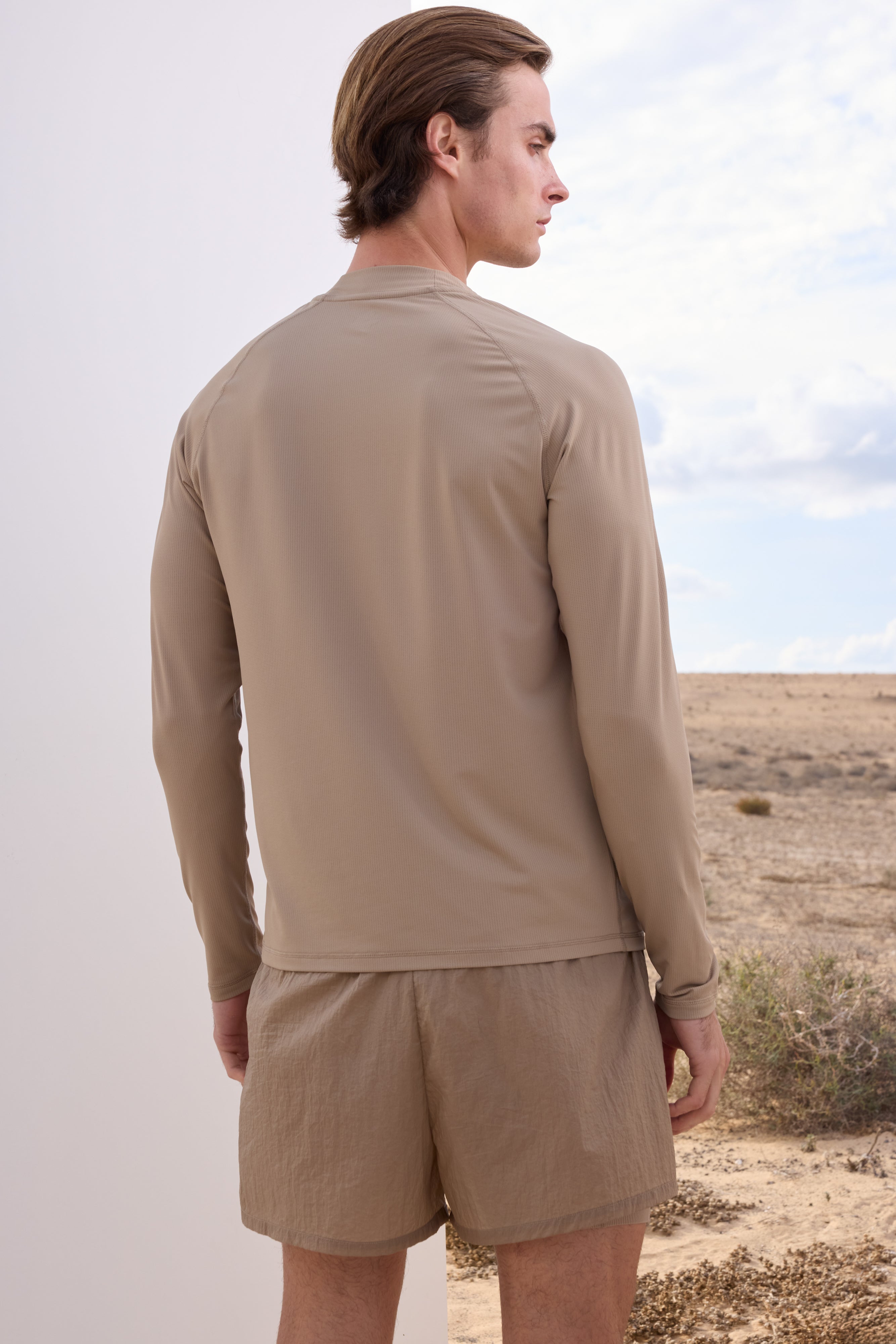 Man wearing a beige long-sleeve t-shirt and shorts set in a desert landscape.
