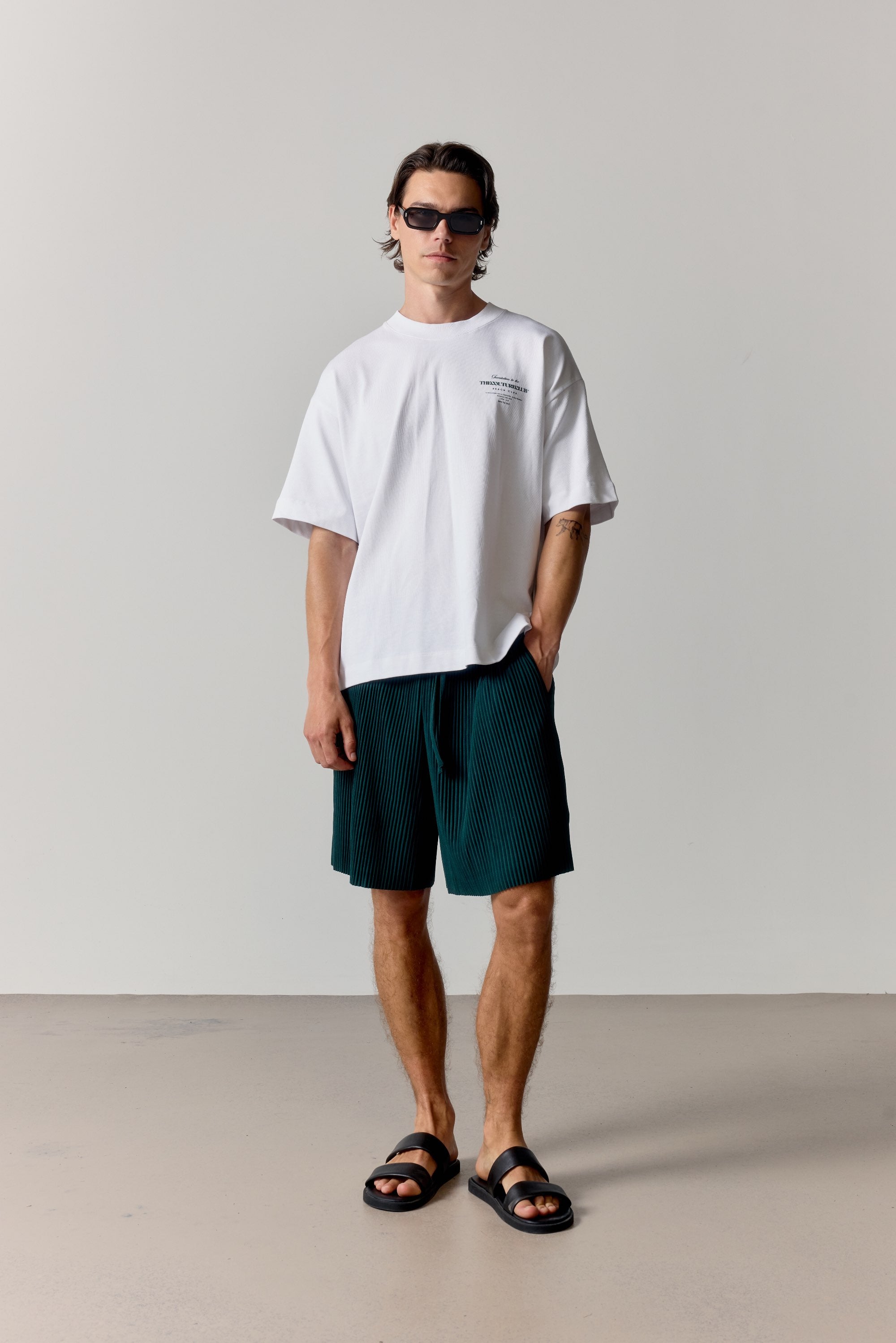 Man wearing a white t-shirt and dark green shorts standing against a plain background