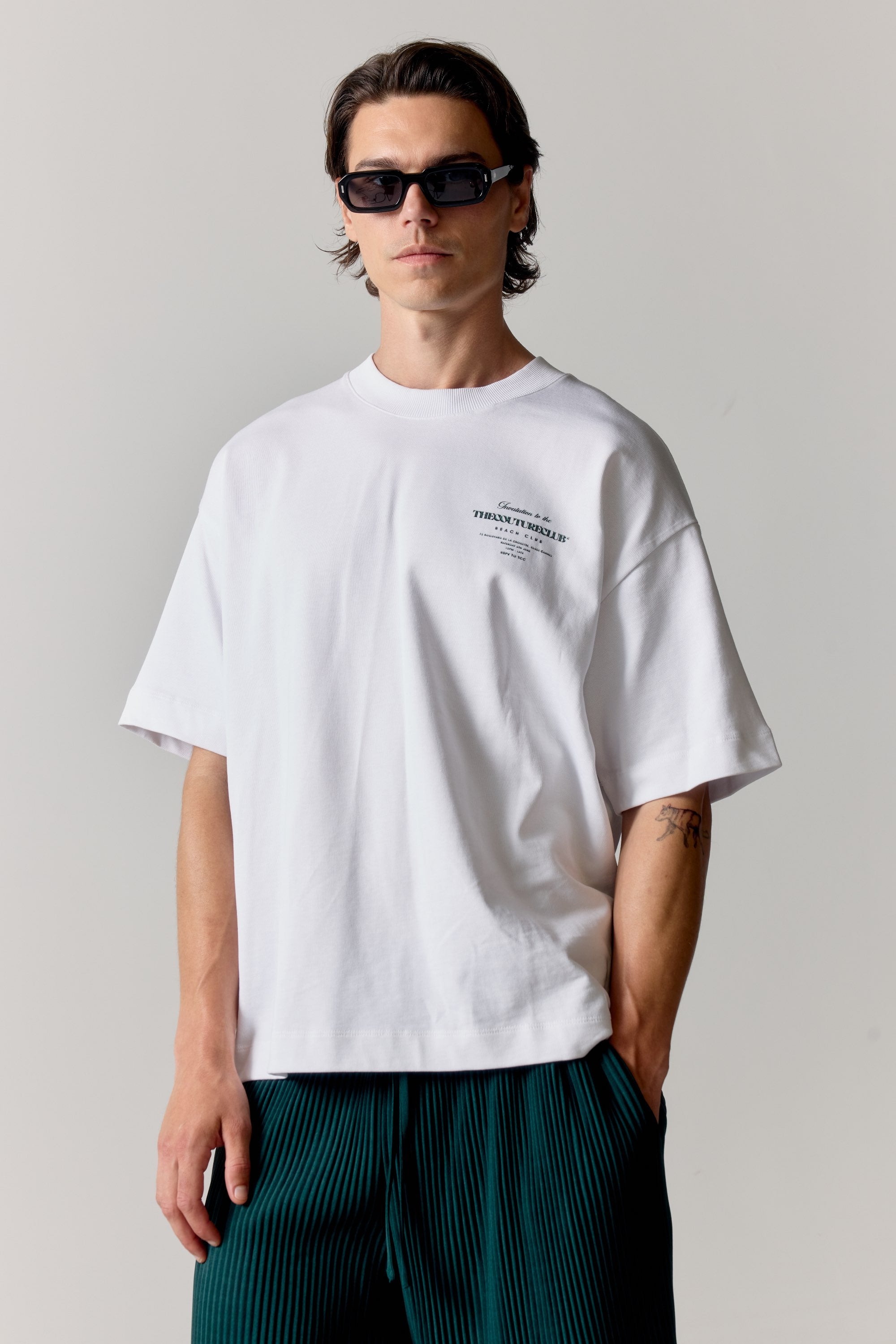 Man wearing a white t-shirt with text and dark sunglasses against a plain background