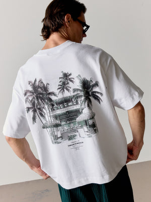 Person wearing a white t-shirt with a green graphic design on the back, standing against a plain background.
