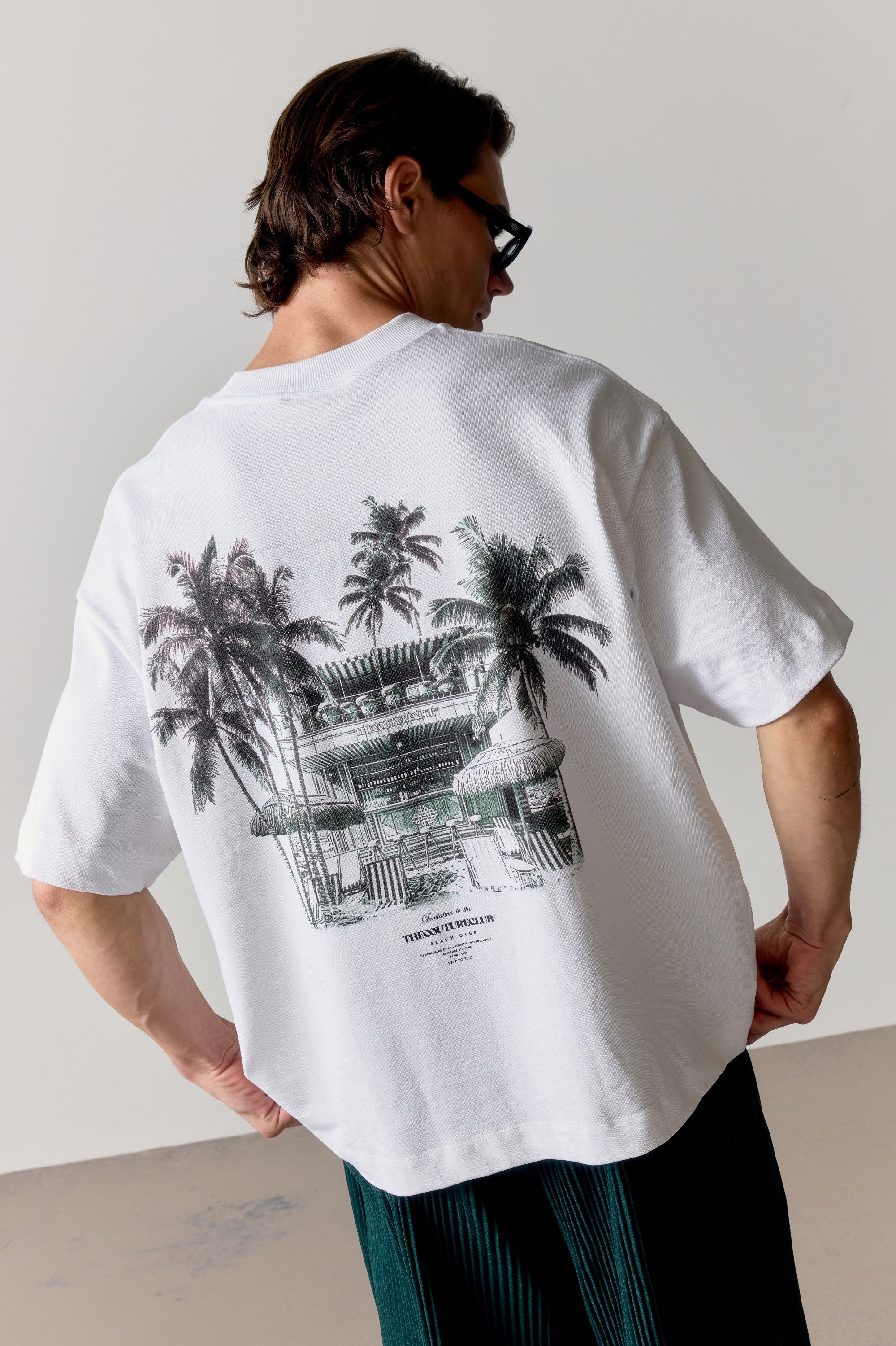 Person wearing a white t-shirt with a green graphic design on the back, standing against a plain background.