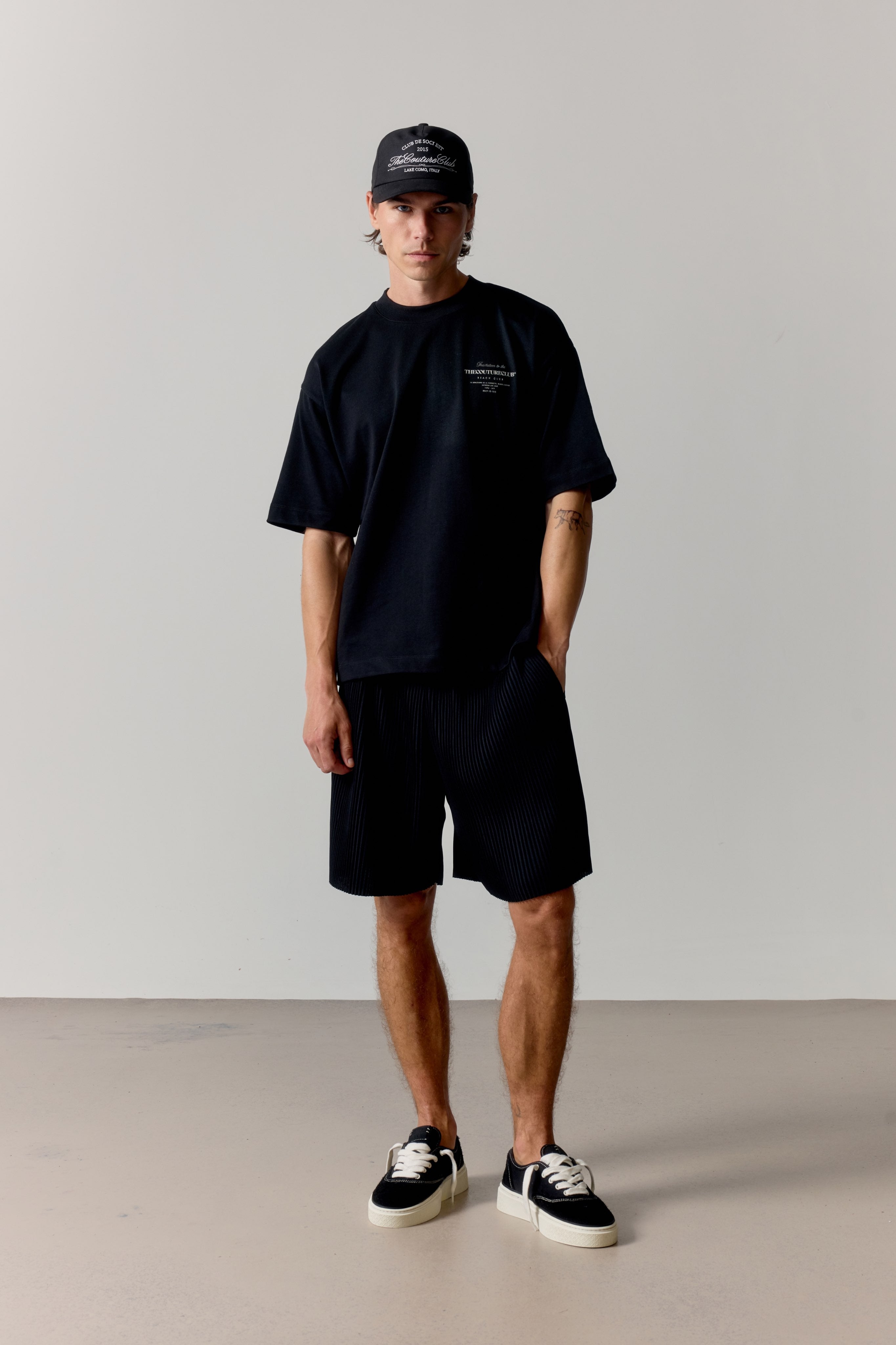 Person wearing a black t-shirt, shorts, and cap on a plain background