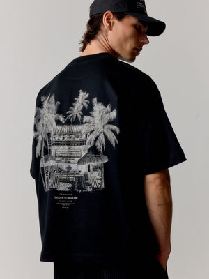 Person wearing a black t-shirt with palm tree and building graphic on a plain background