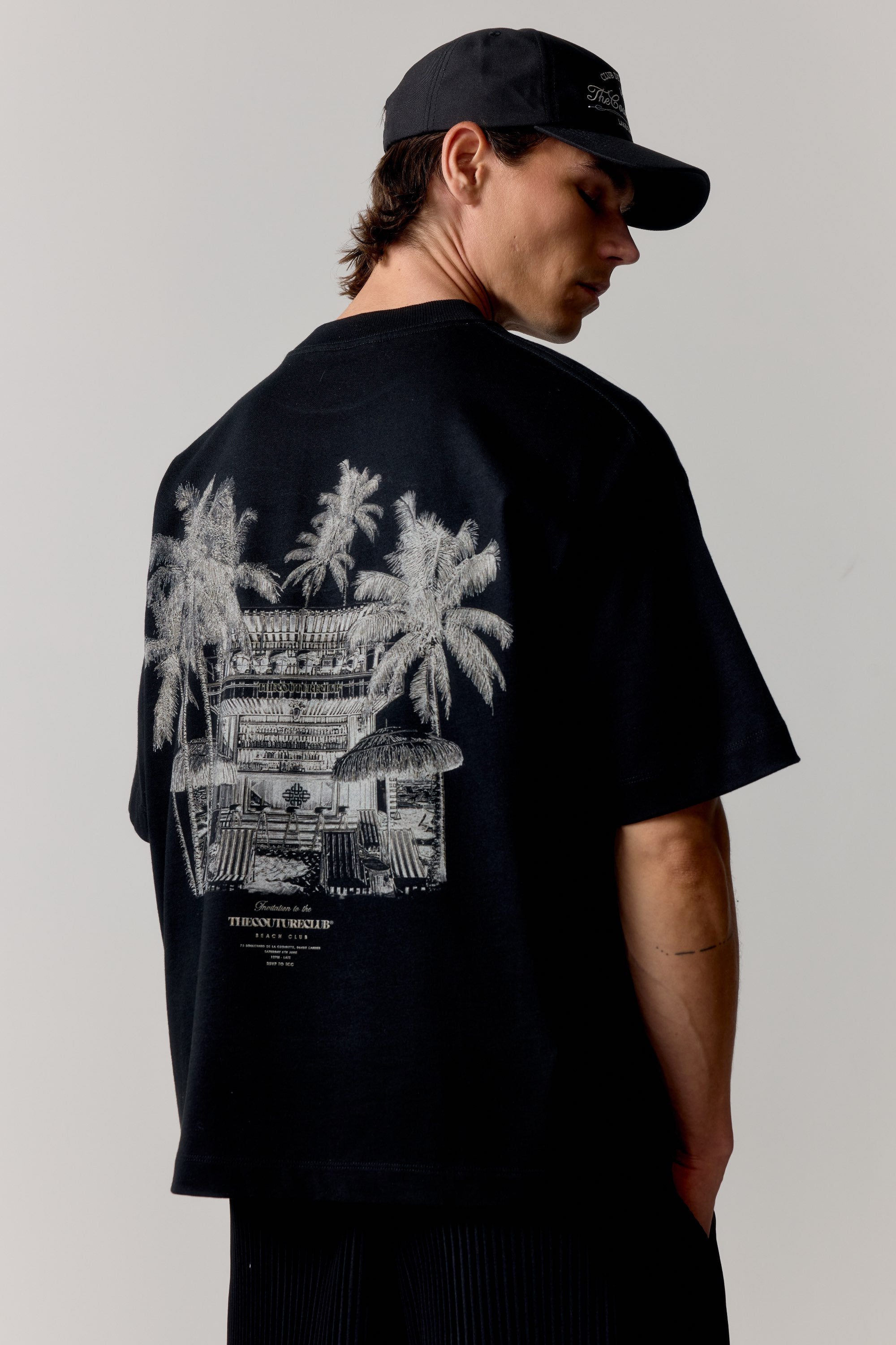 Person wearing a black t-shirt with palm tree and building graphic on a plain background