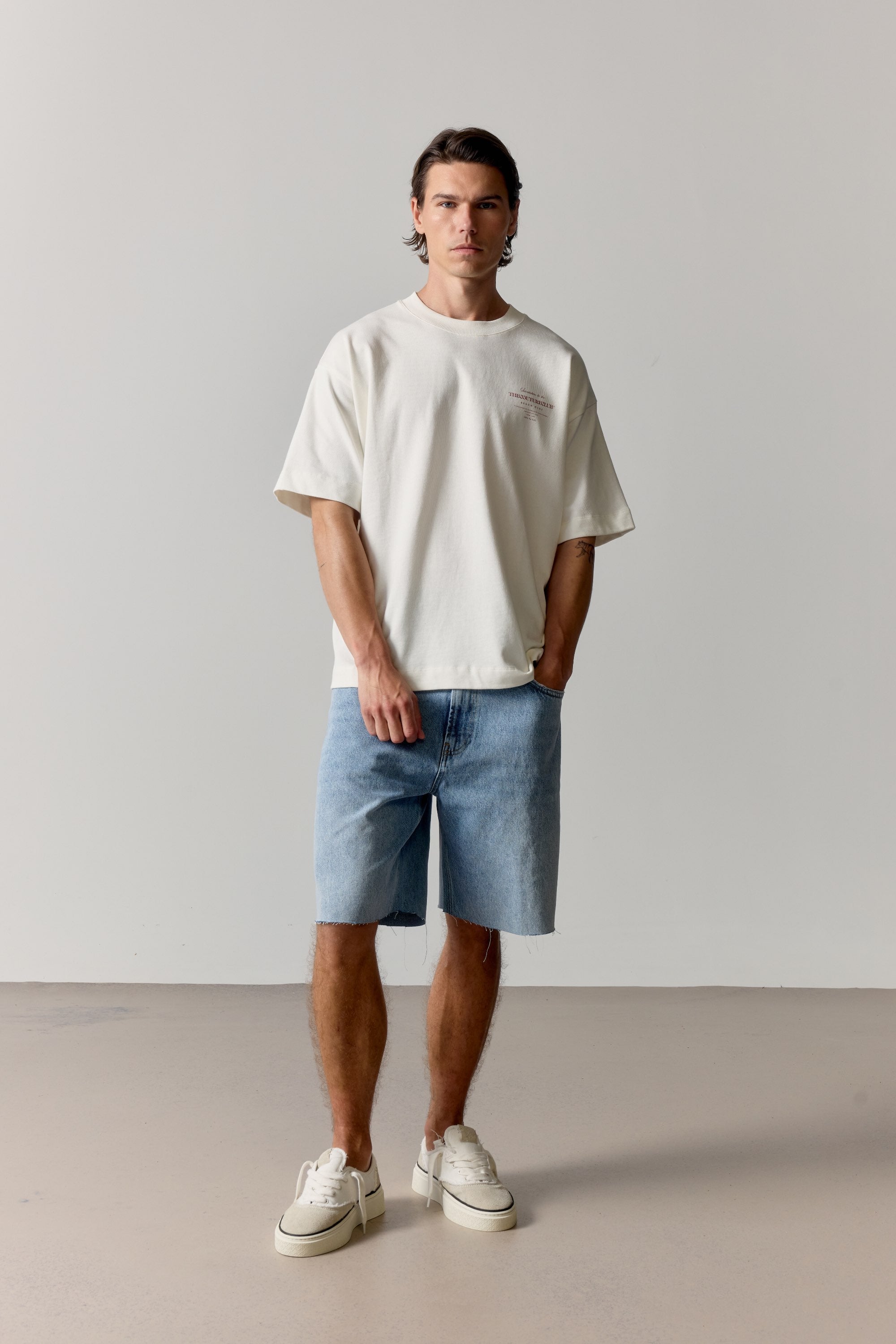 Man wearing a white t-shirt and light blue shorts against a plain background