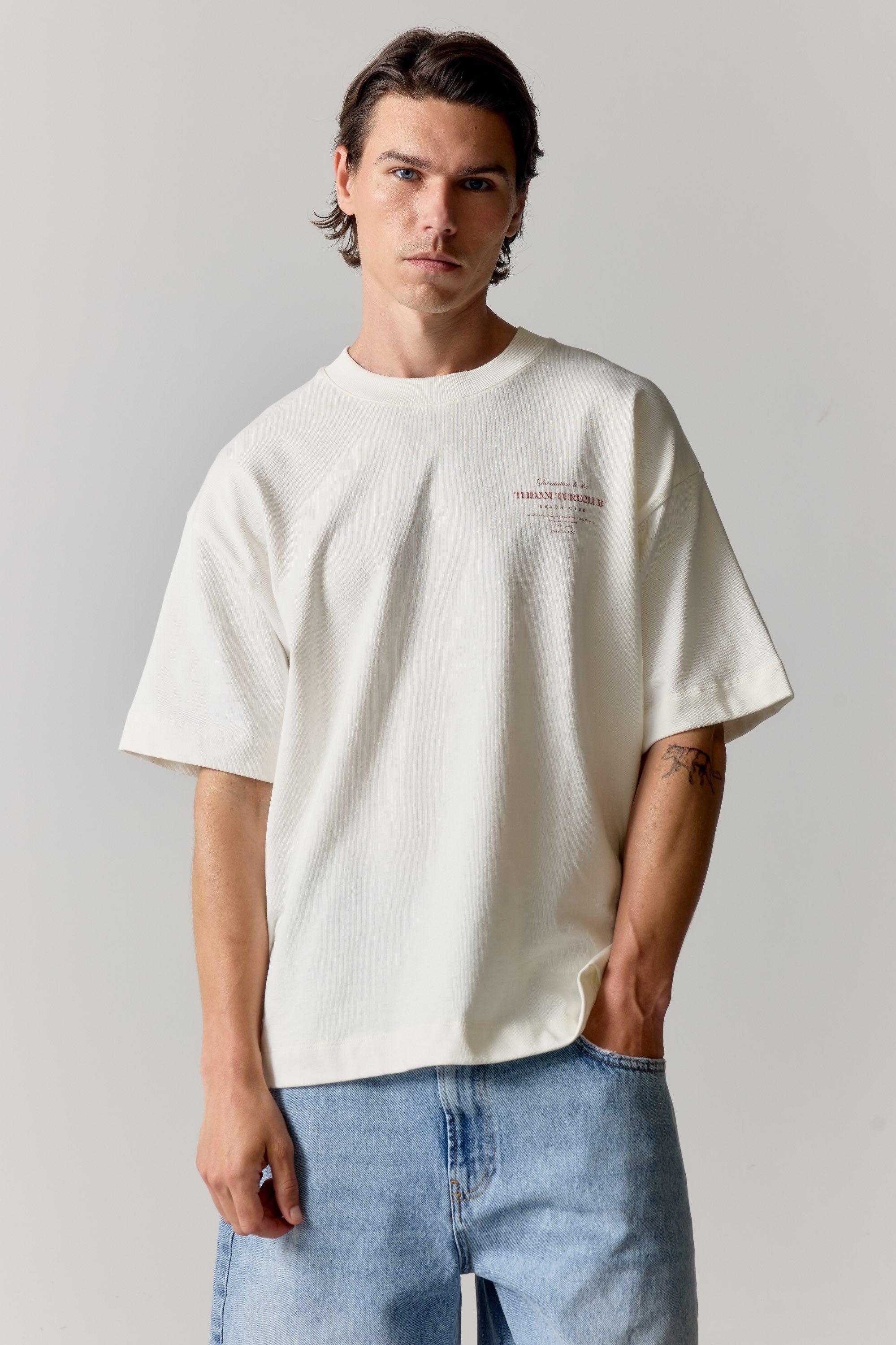 Man wearing a white t-shirt with pink text and blue jeans on a plain background