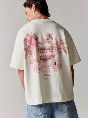Person wearing a white t-shirt with pink graphic design on the back, standing against a plain background.