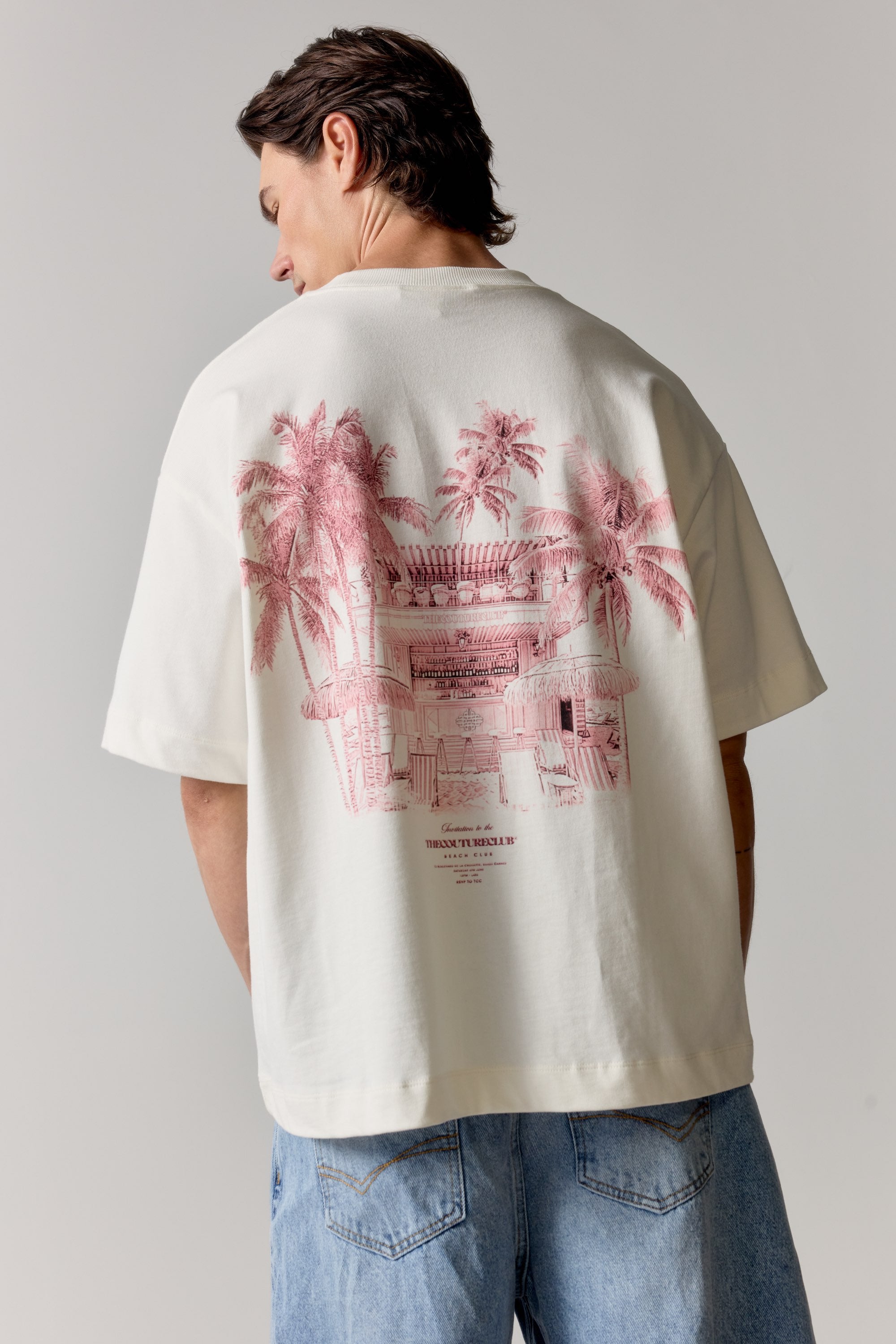 Person wearing a white t-shirt with pink graphic design on the back, standing against a plain background.