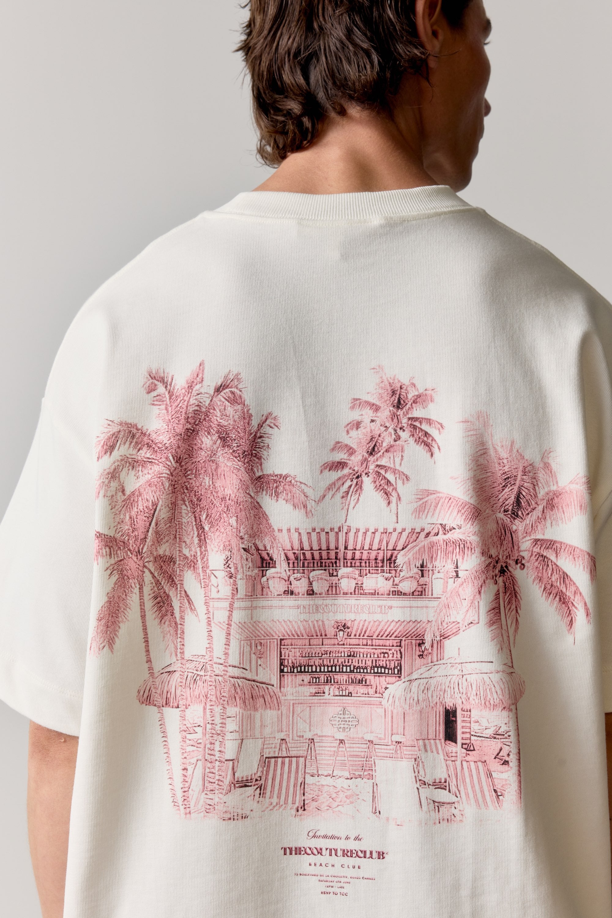Person wearing a white t-shirt with pink palm tree and building design on the back.