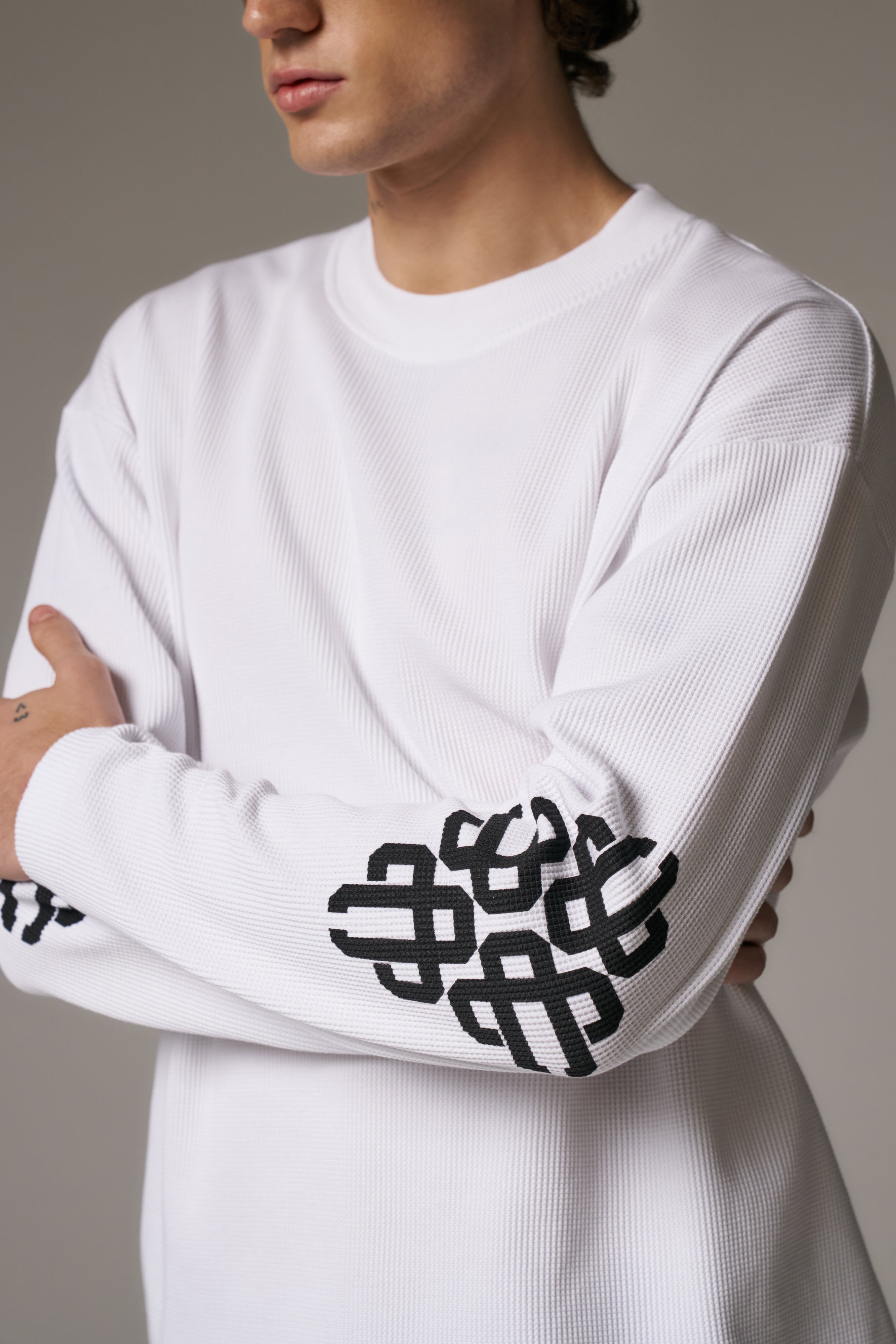 Person wearing a white long-sleeve shirt with black geometric patterns on the sleeves against a neutral background