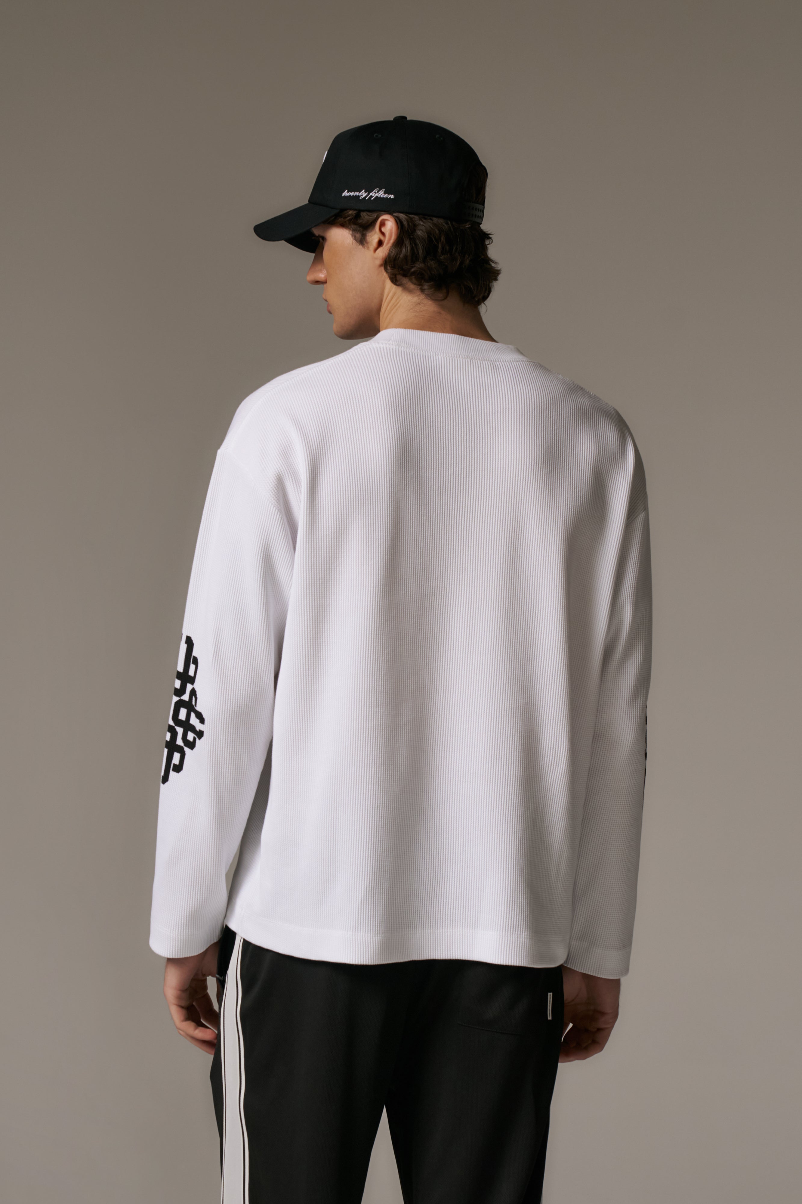 Person wearing a white long-sleeve t-shirt and black cap on a beige background
