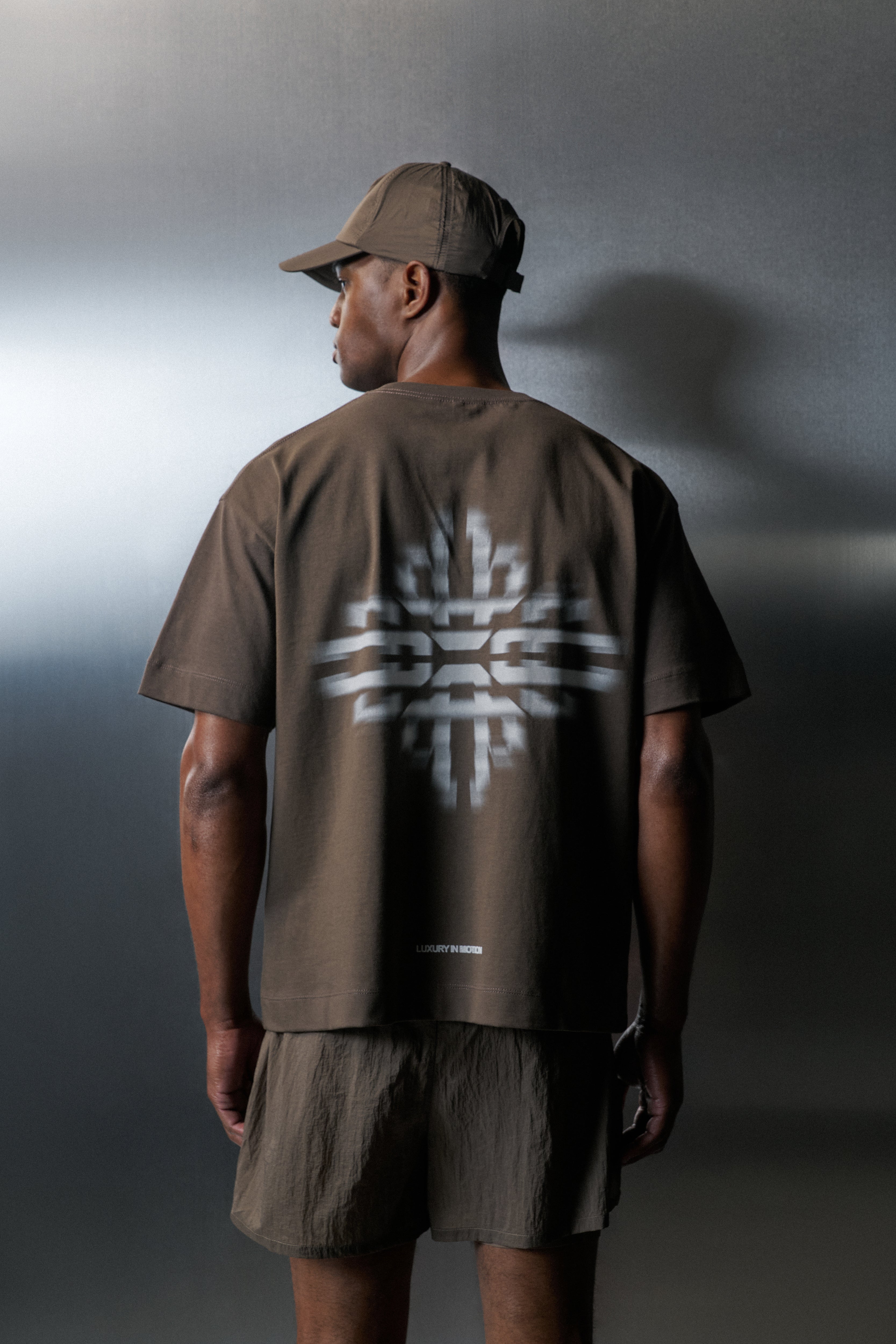 Person wearing a brown t-shirt with a white logo on the back against a grey background