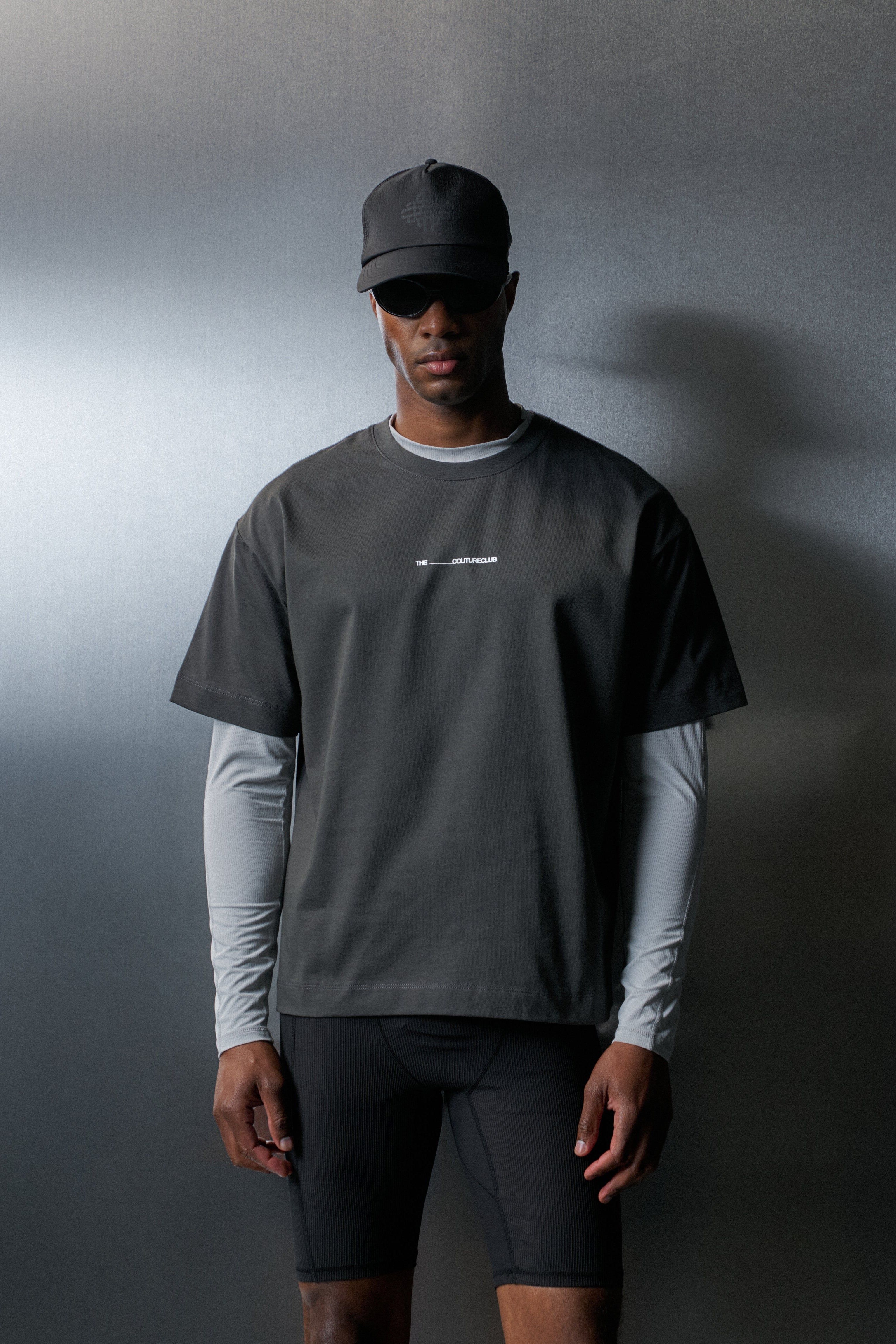 Man wearing a dark grey t-shirt with long-sleeve underneath and black cap against a gradient background