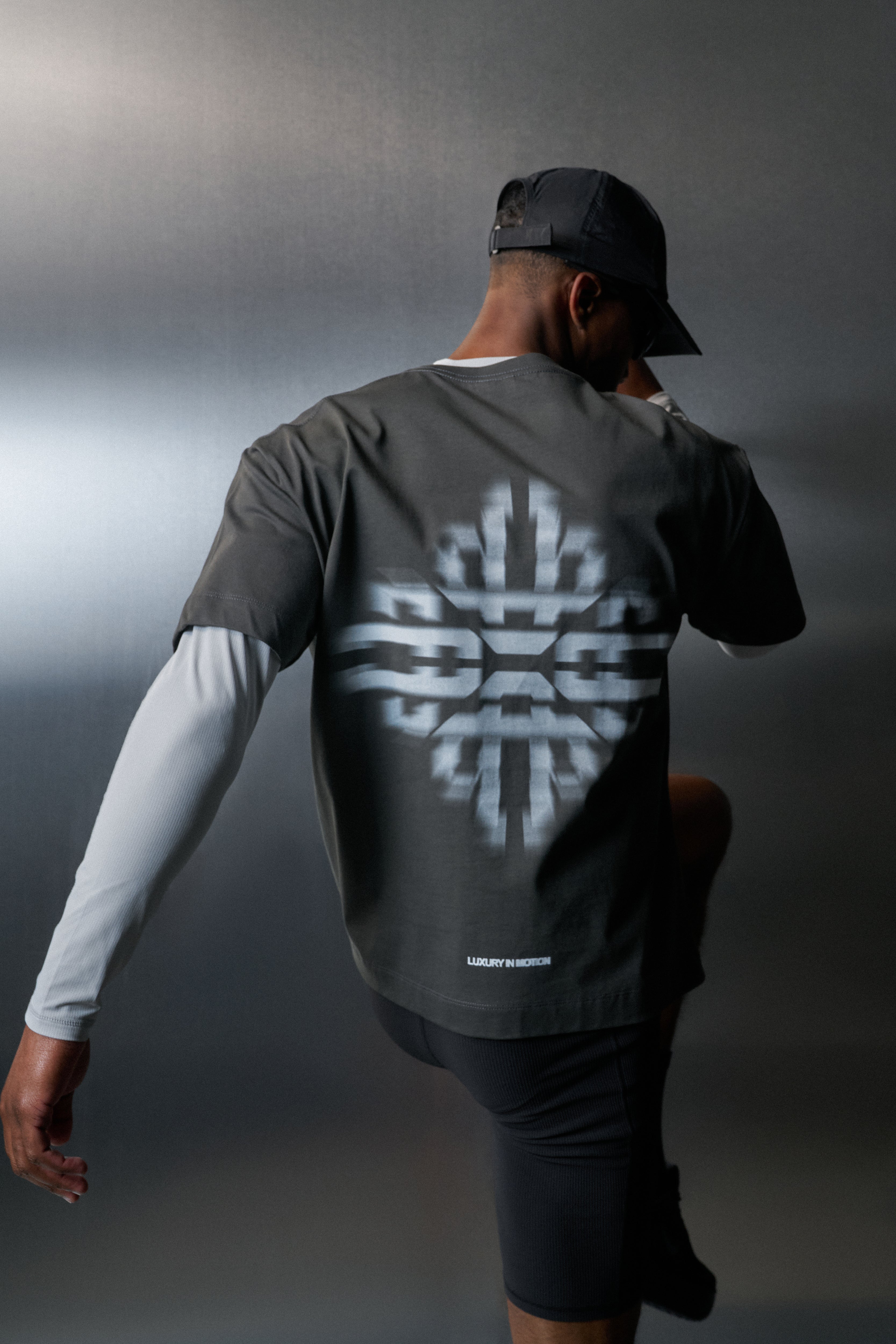 Person wearing a dark grey  t-shirt with a white geometric design on the back, standing against a dark background.