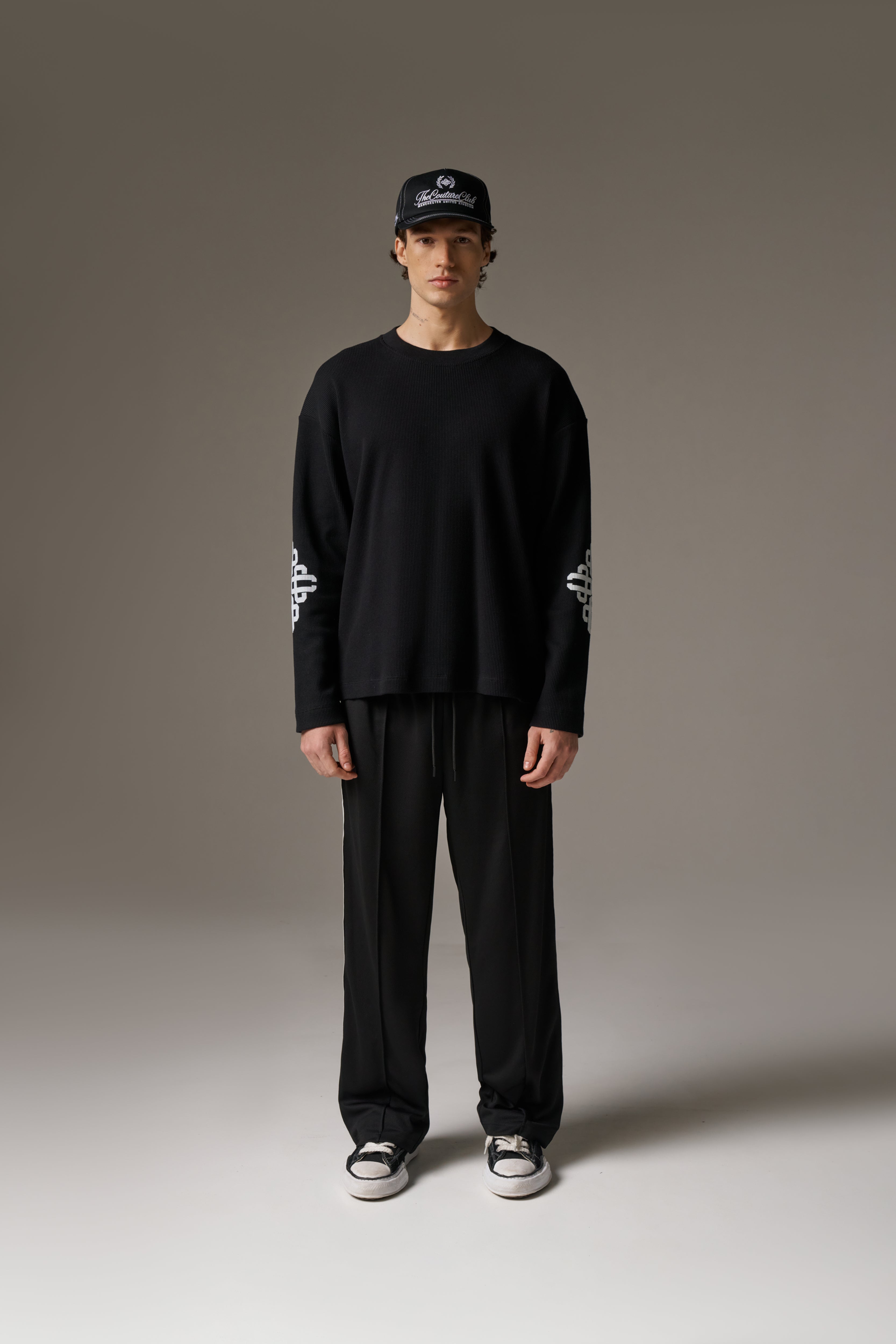Person wearing a black outfit with white text on sleeves against a neutral background