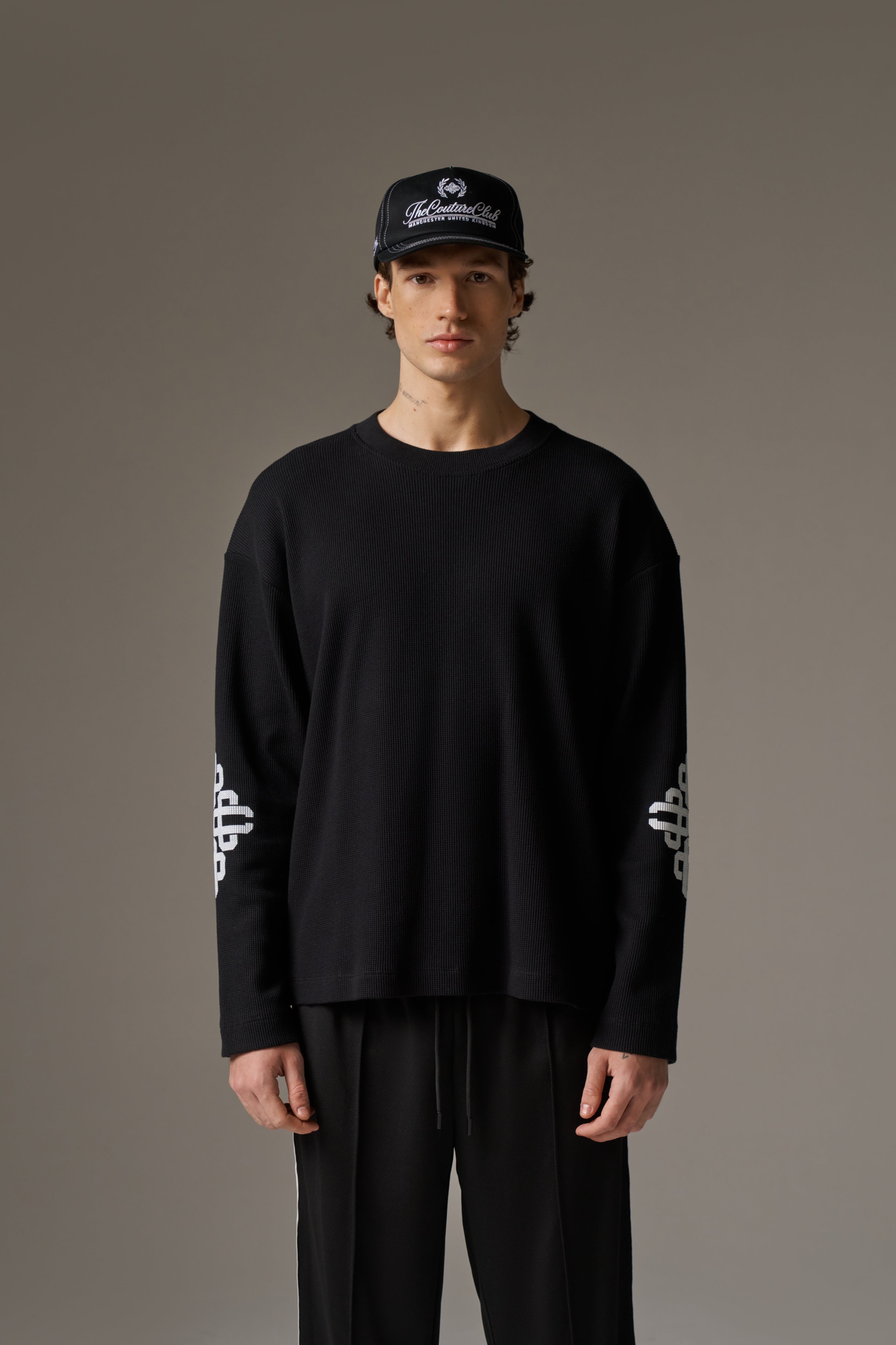 Person wearing a black outfit with white artwork on sleeves against a grey background