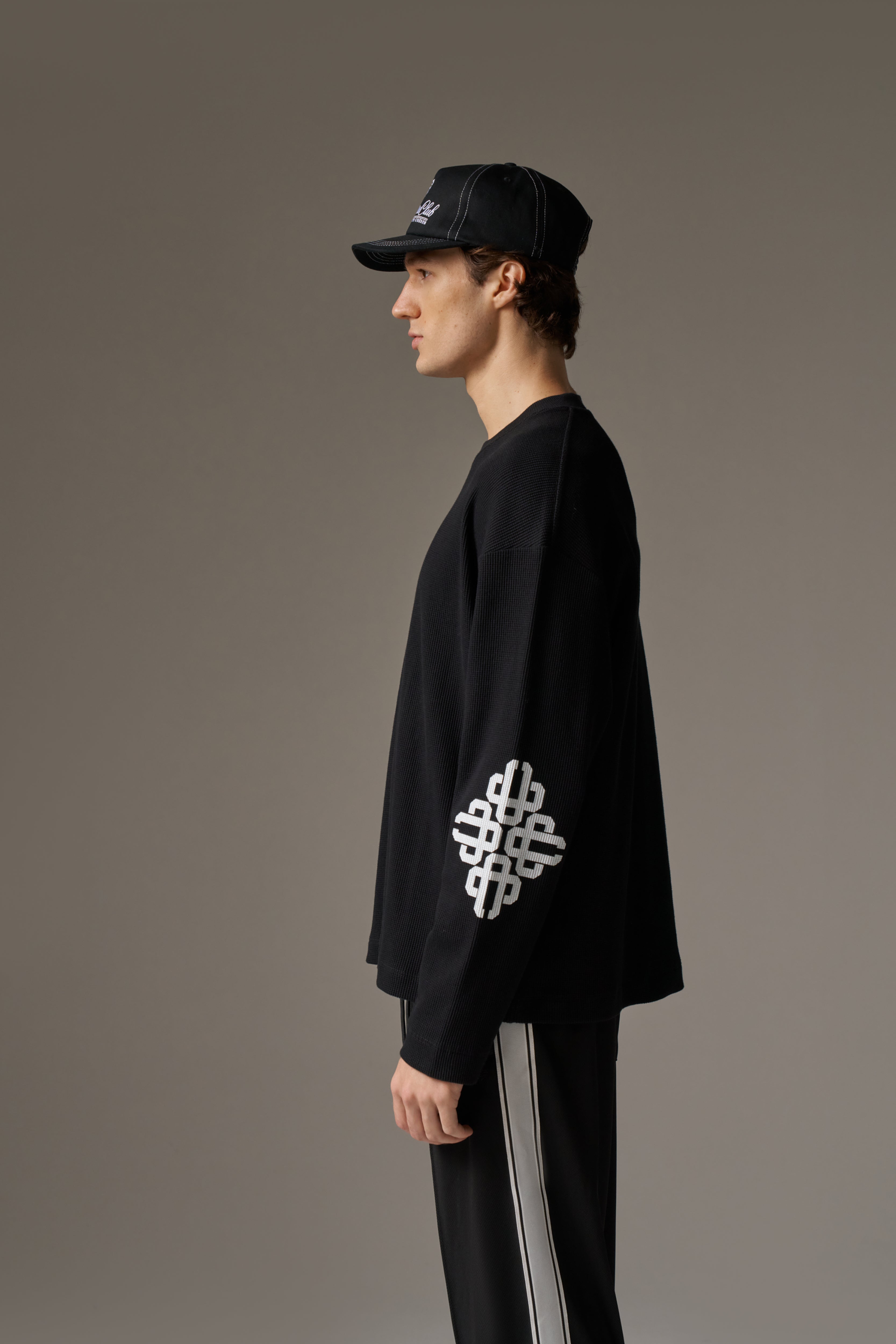 Person wearing a black outfit with a distinctive white design on a grey background