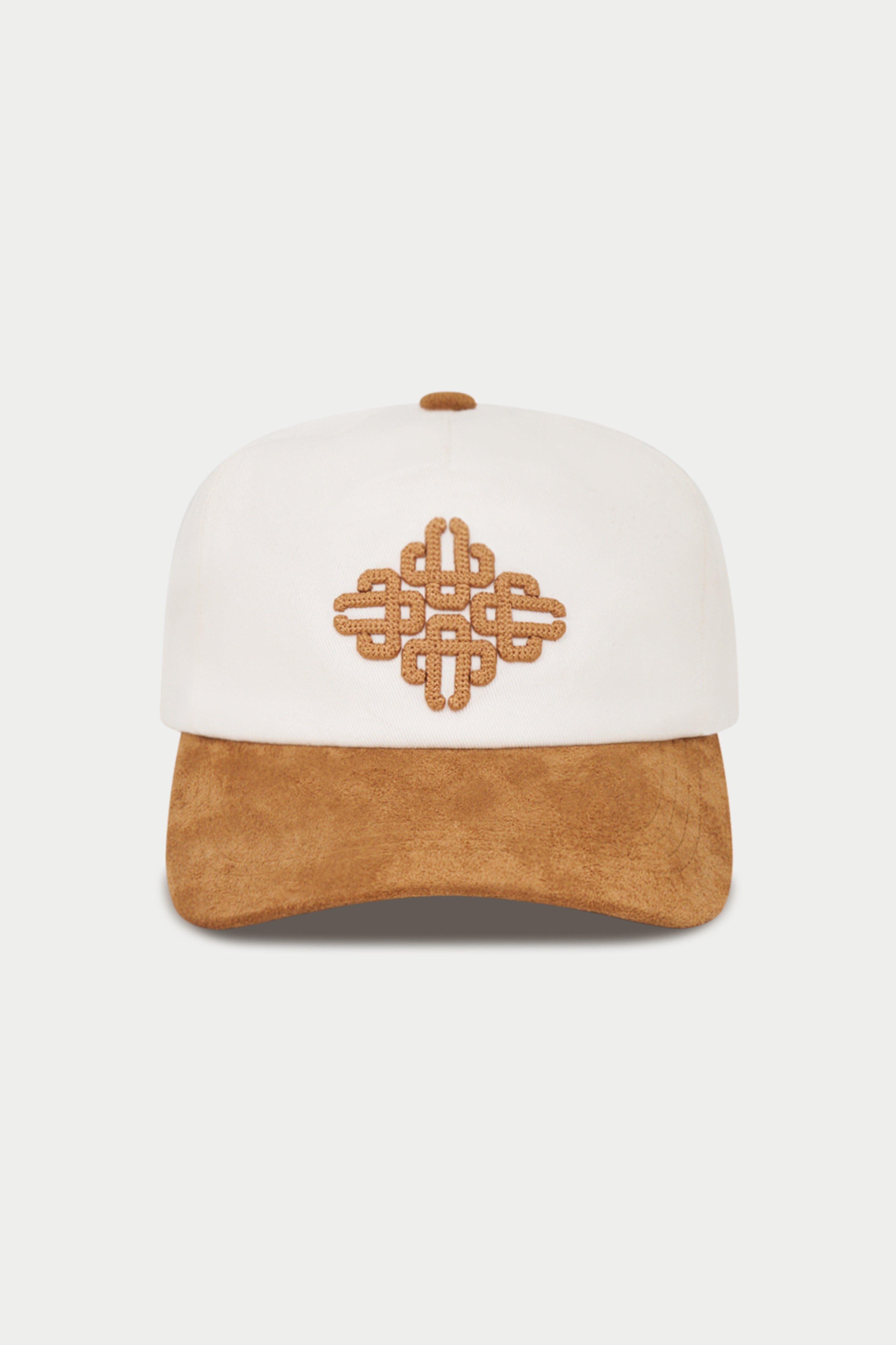 A structured baseball cap with an off-white crown and a tan suede-look curved brim, featuring a matching tan embroidered geometric knot motif on the front.