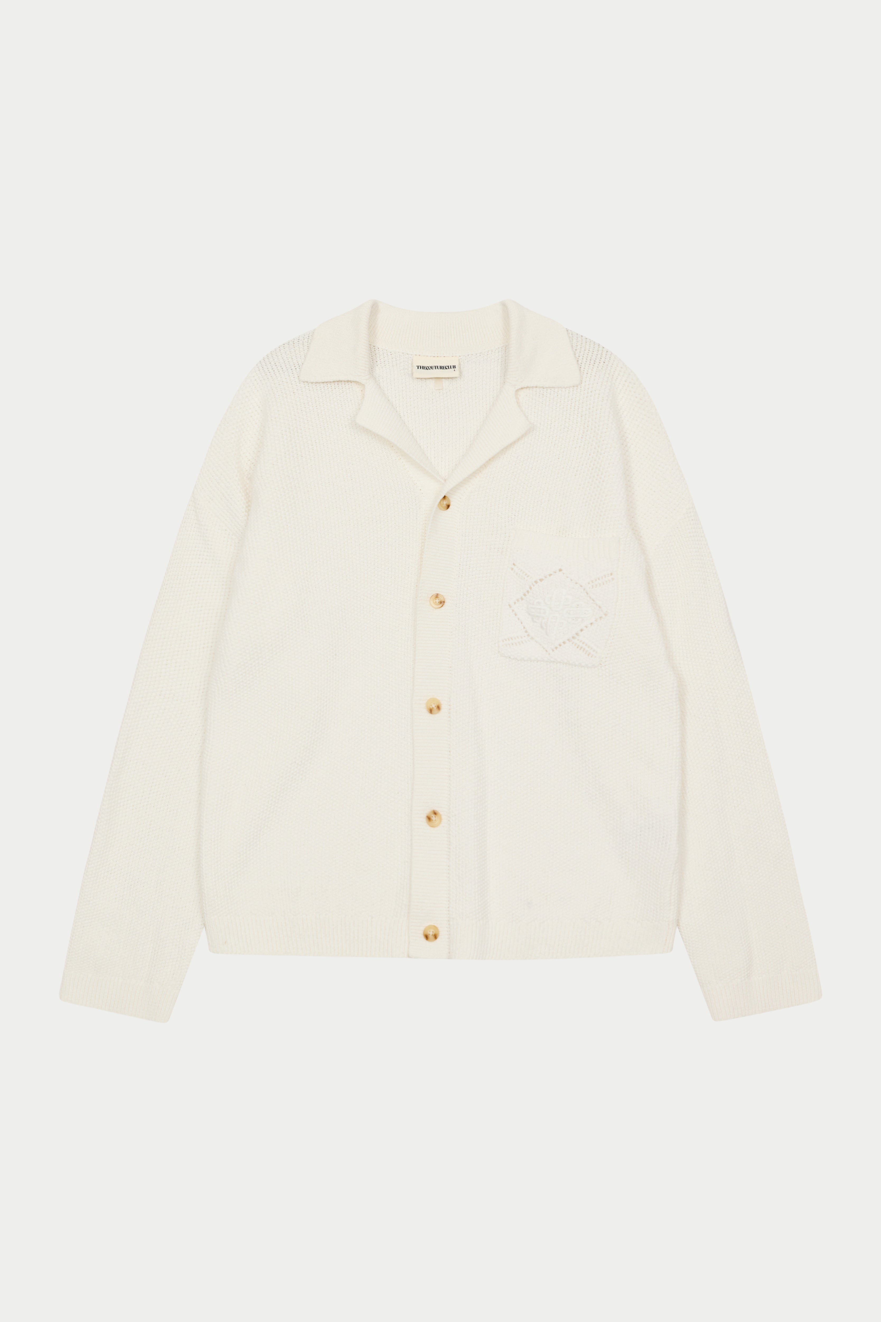 A long-sleeved off white shirt with a ribbed revere collar, crochet knit fabric, and a front left chest patch pocket with an embroidered emblem.