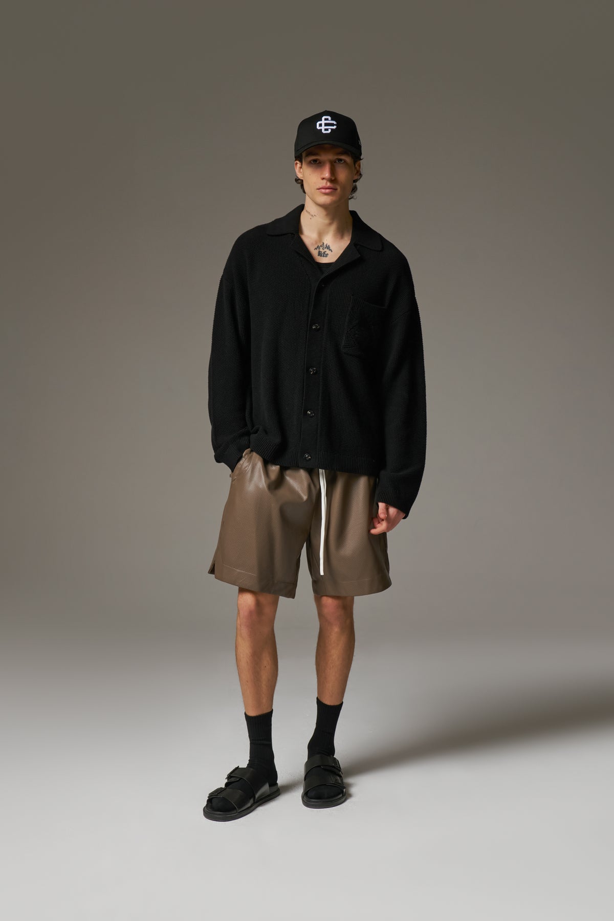 A person wearing a long-sleeved black shirt with a ribbed collar, crochet knit fabric, and an embroidered emblem on the chest pocket.