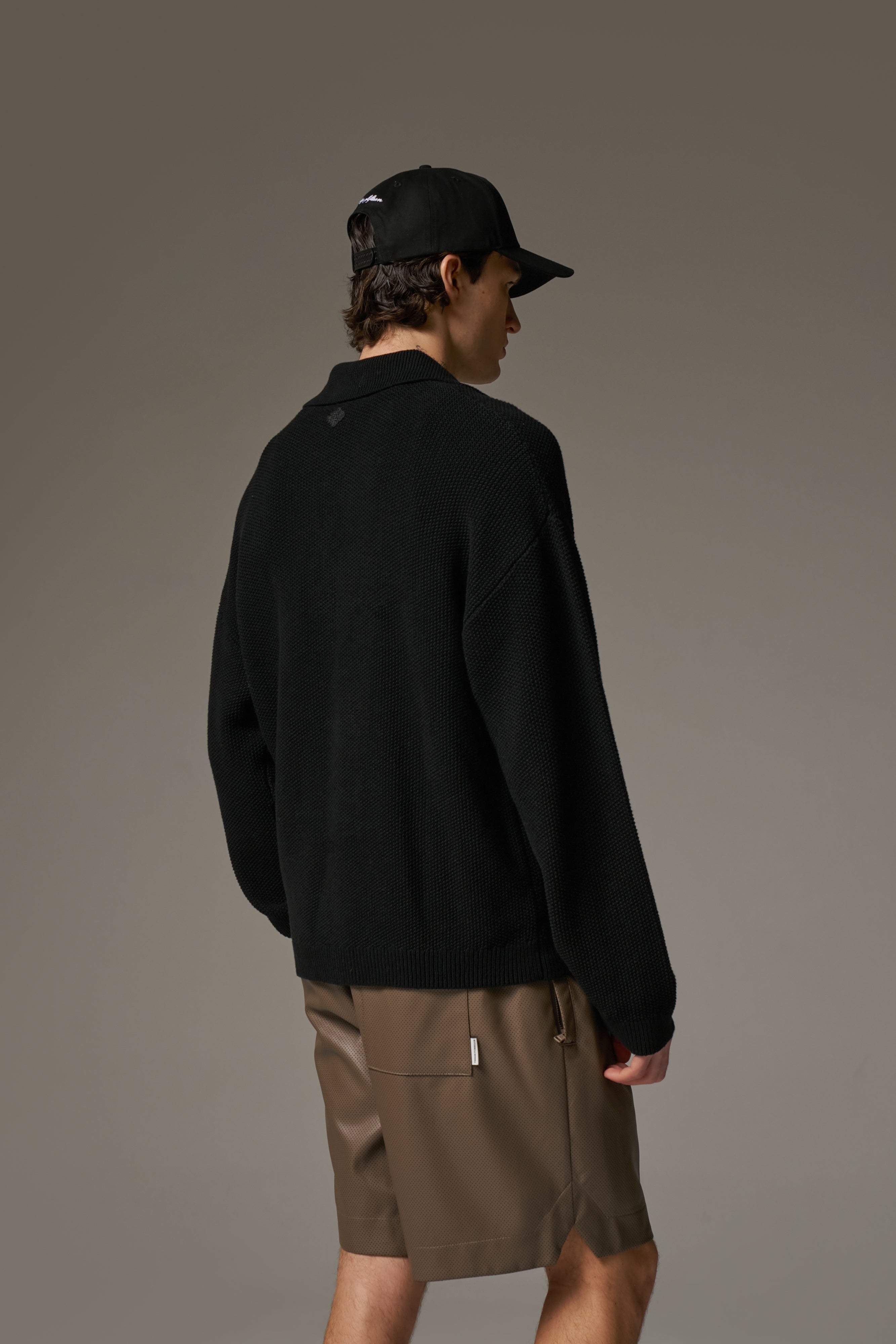 Back view of a person wearing a long-sleeved black shirt  and a black baseball cap and brown leather shorts.