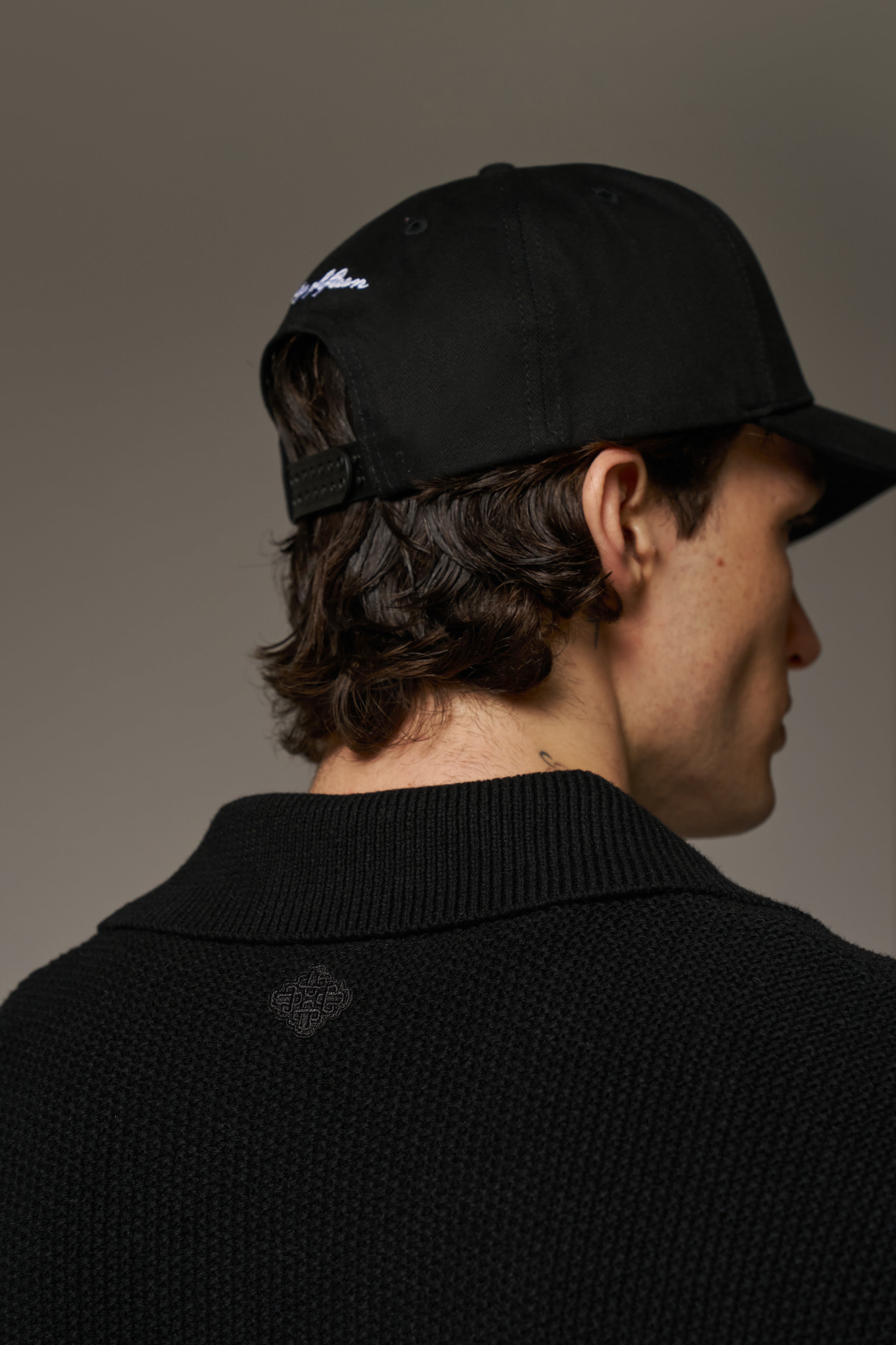 Close up detail shot of the back of a person wearing a long-sleeved black shirt  and a black baseball cap.