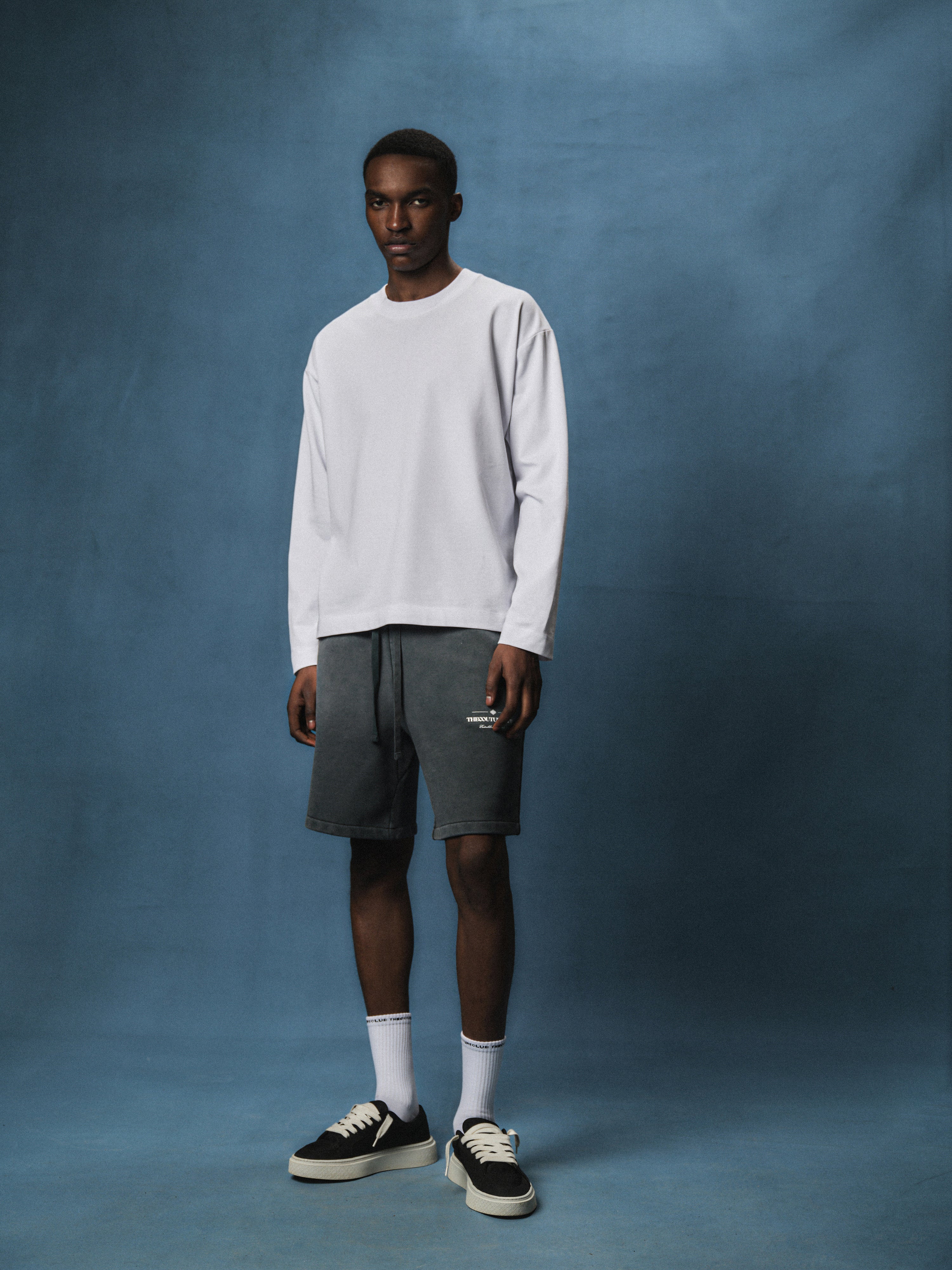 Person wearing a white long sleeved t-shirt and grey shorts against a blue background