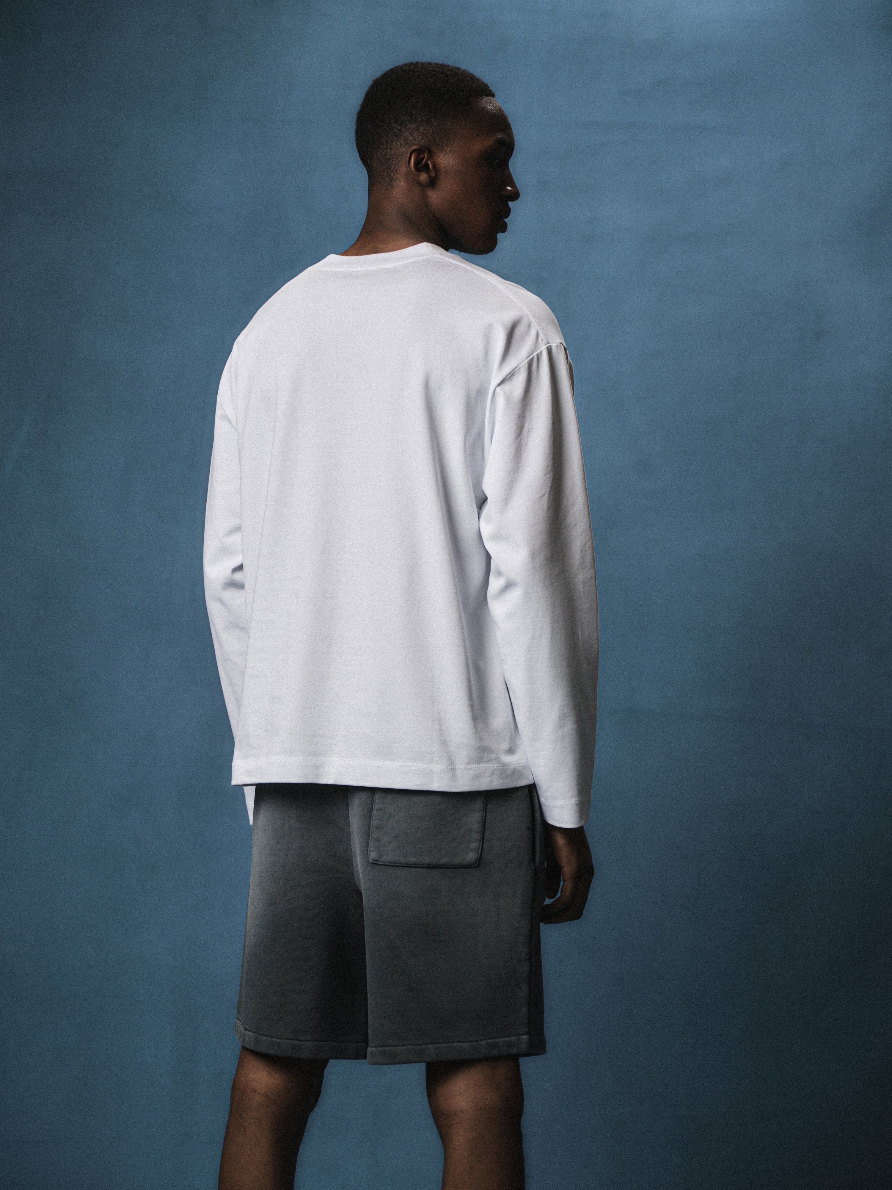 Person wearing a white long-sleeve t-shirt and grey shorts against a blue background