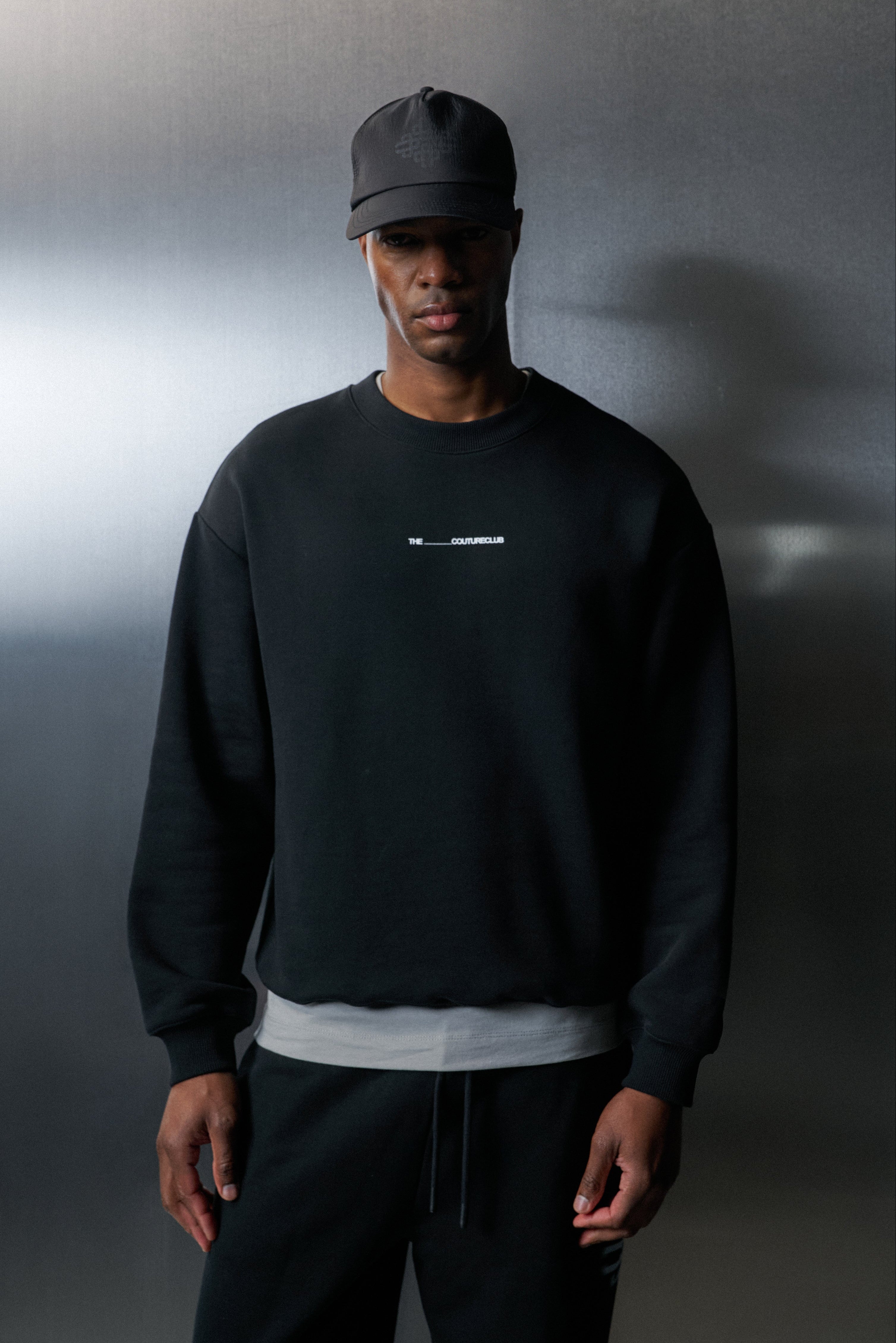 Person wearing a black sweatshirt and cap against a dark background